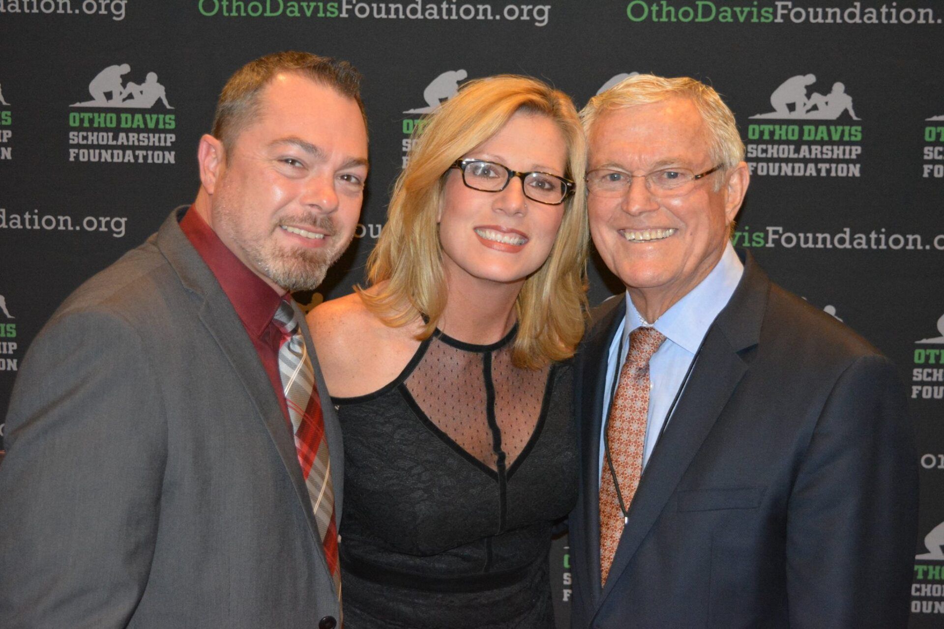 Two men and a woman are posing for a picture in front of a sign that says utah davis scholarship foundation