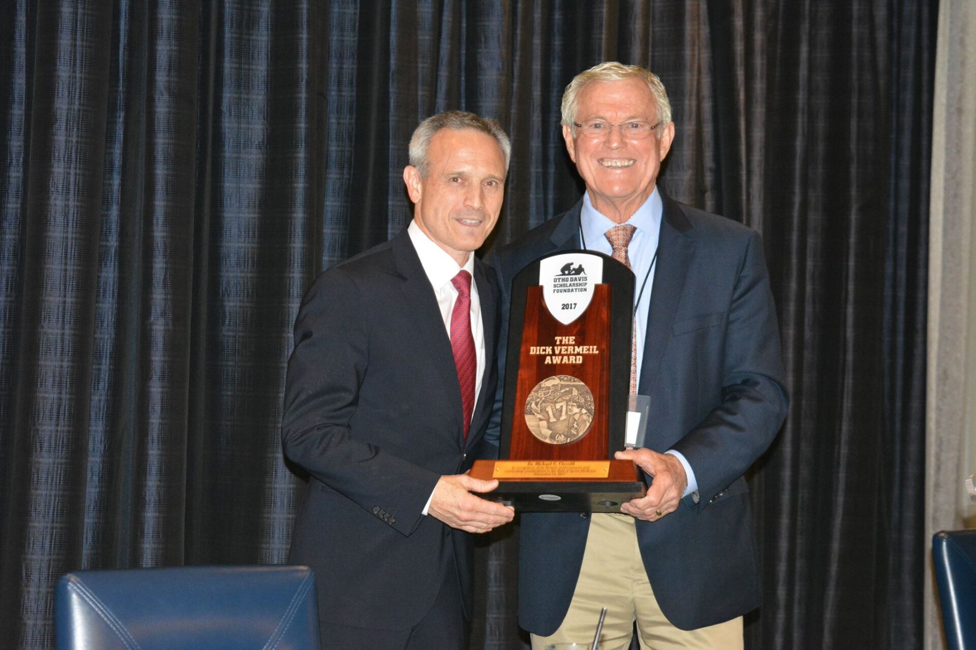 Two men are standing next to each other holding a trophy