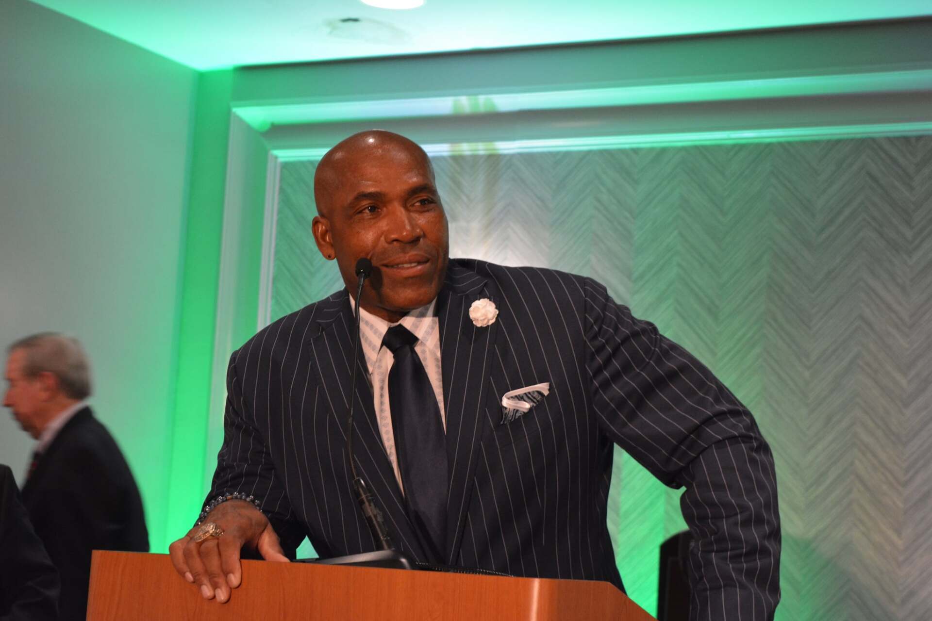 A man in a suit and tie is standing at a podium with a microphone.