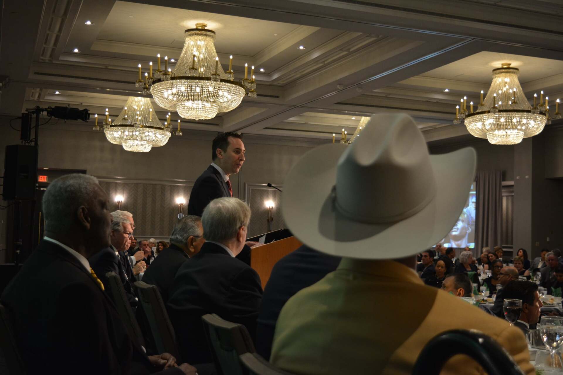 A man in a cowboy hat is giving a speech in front of a crowd.