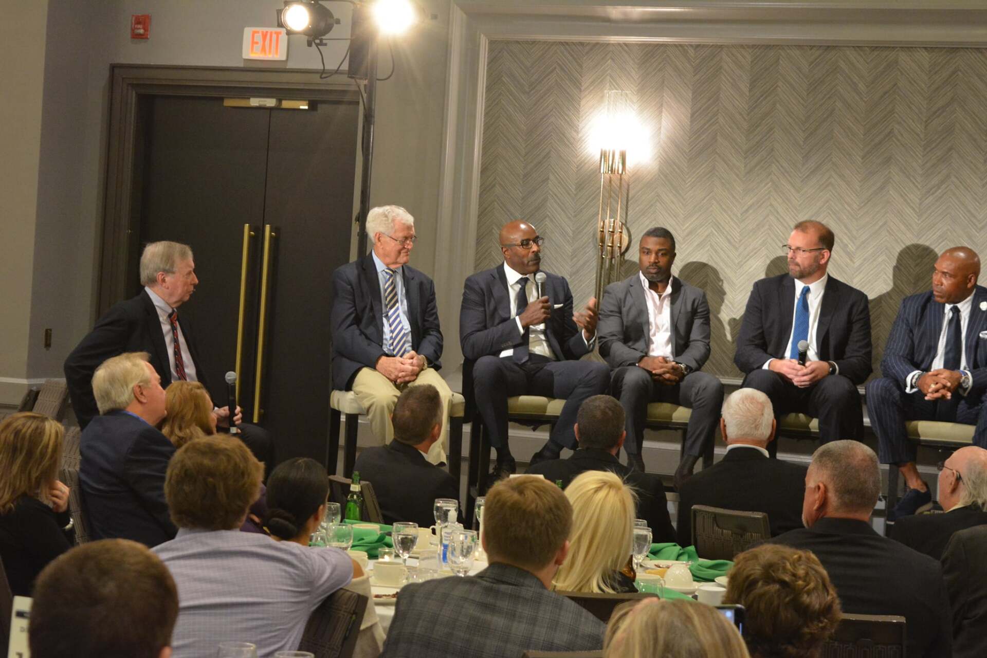 A group of men are sitting on a stage talking to a crowd of people.