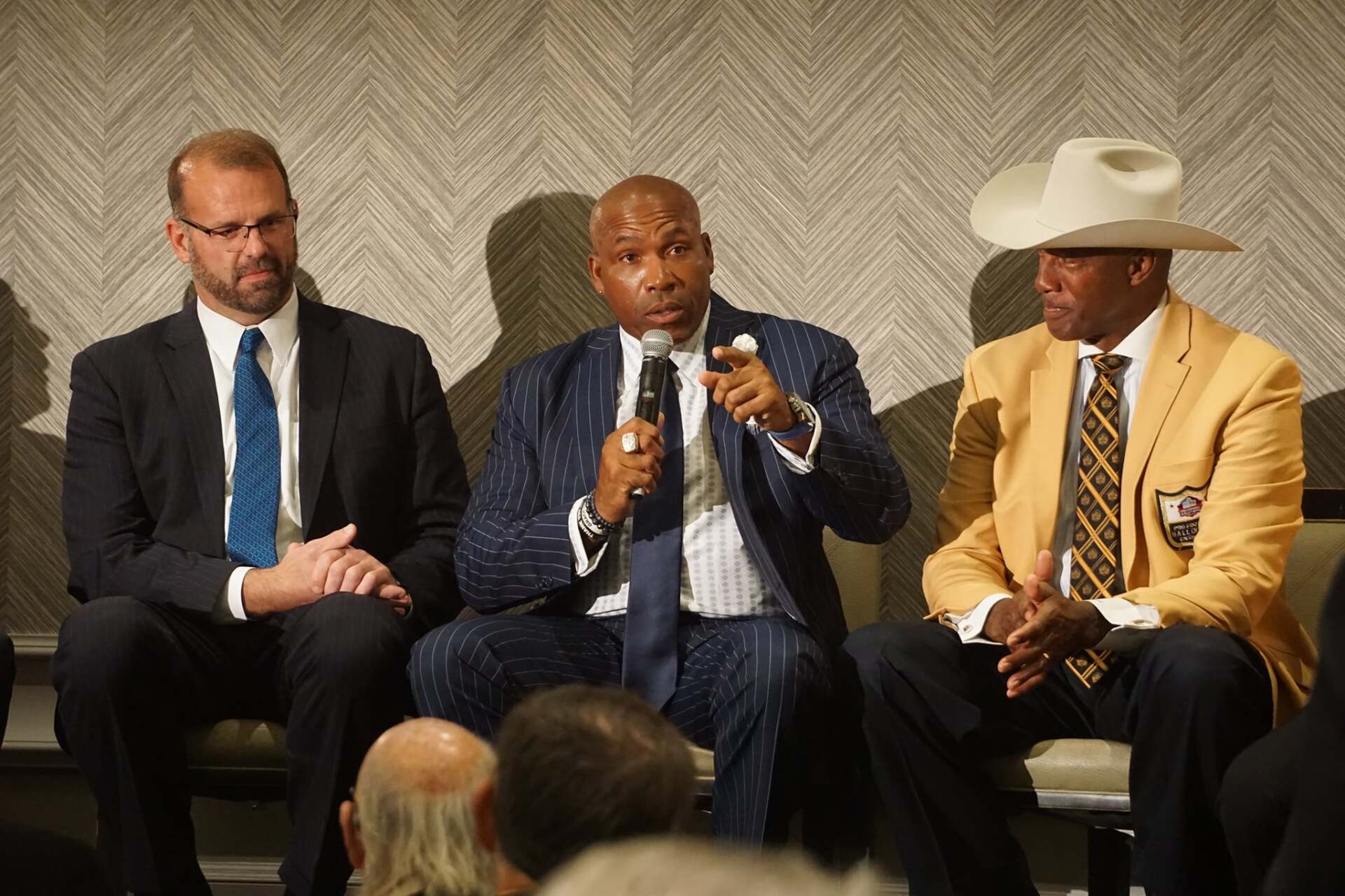 Three men in suits and ties are sitting in a circle talking into microphones.