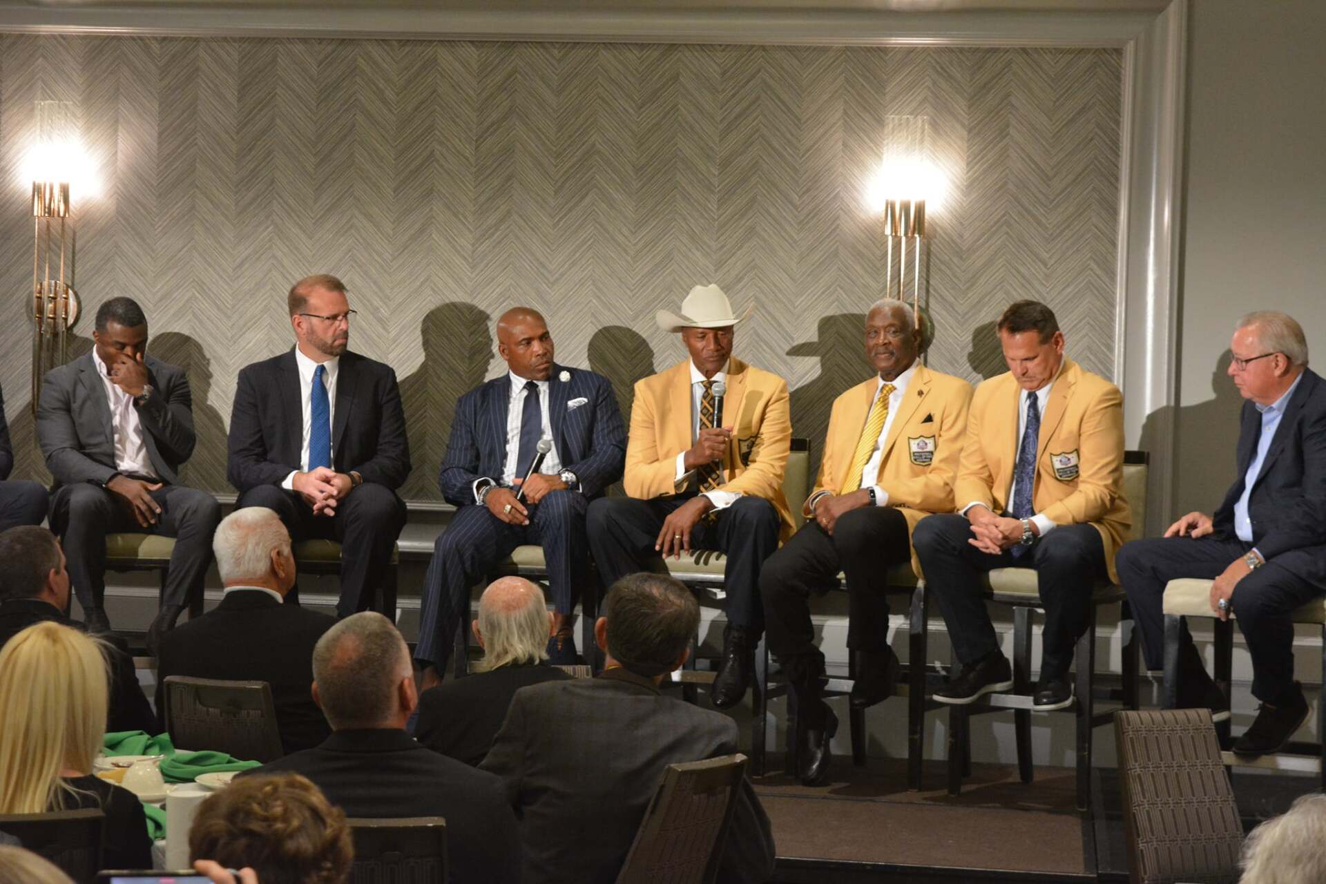 A group of men in suits and ties are sitting in front of a crowd.