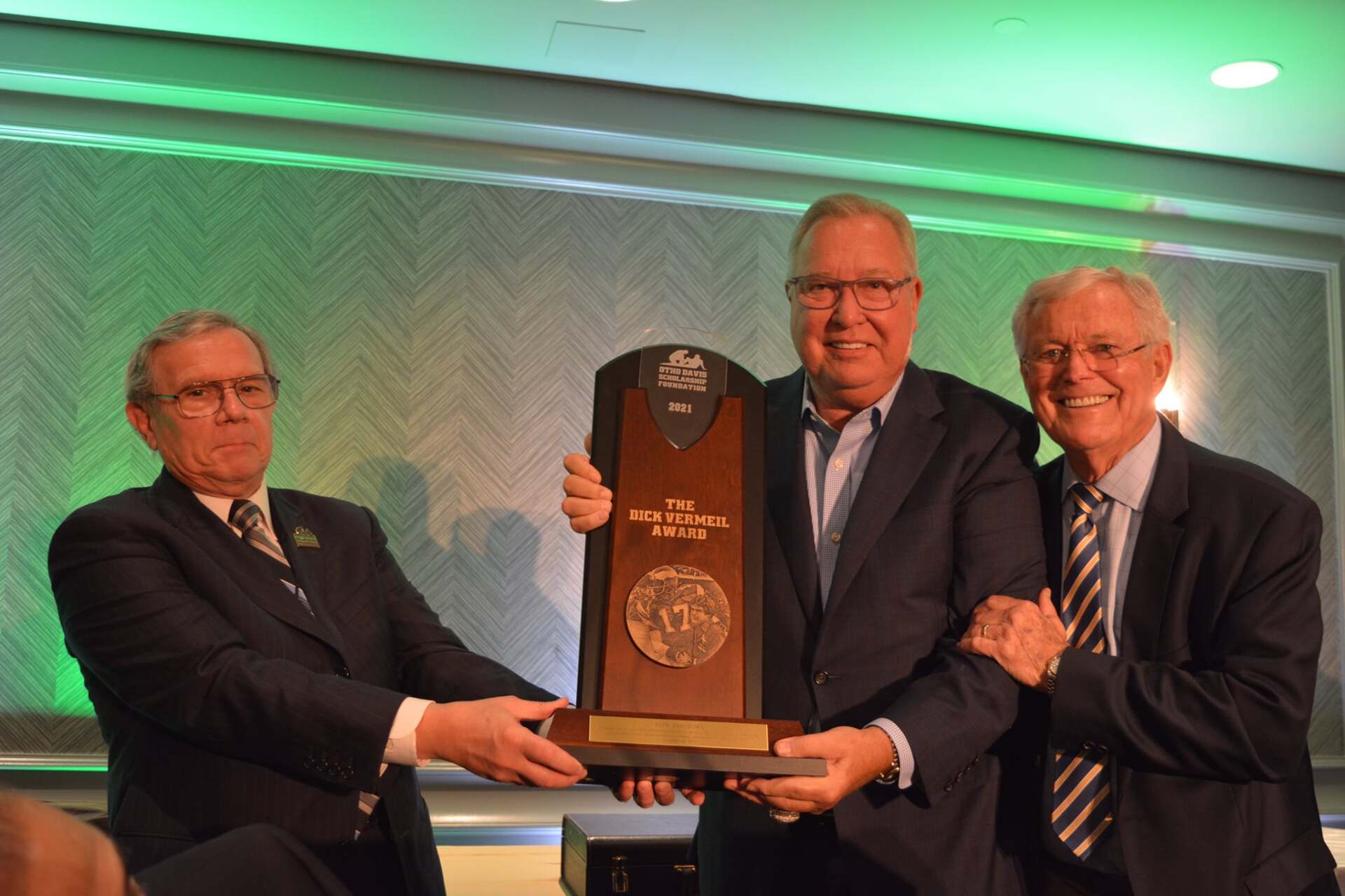 Three men in suits and ties are holding a trophy.