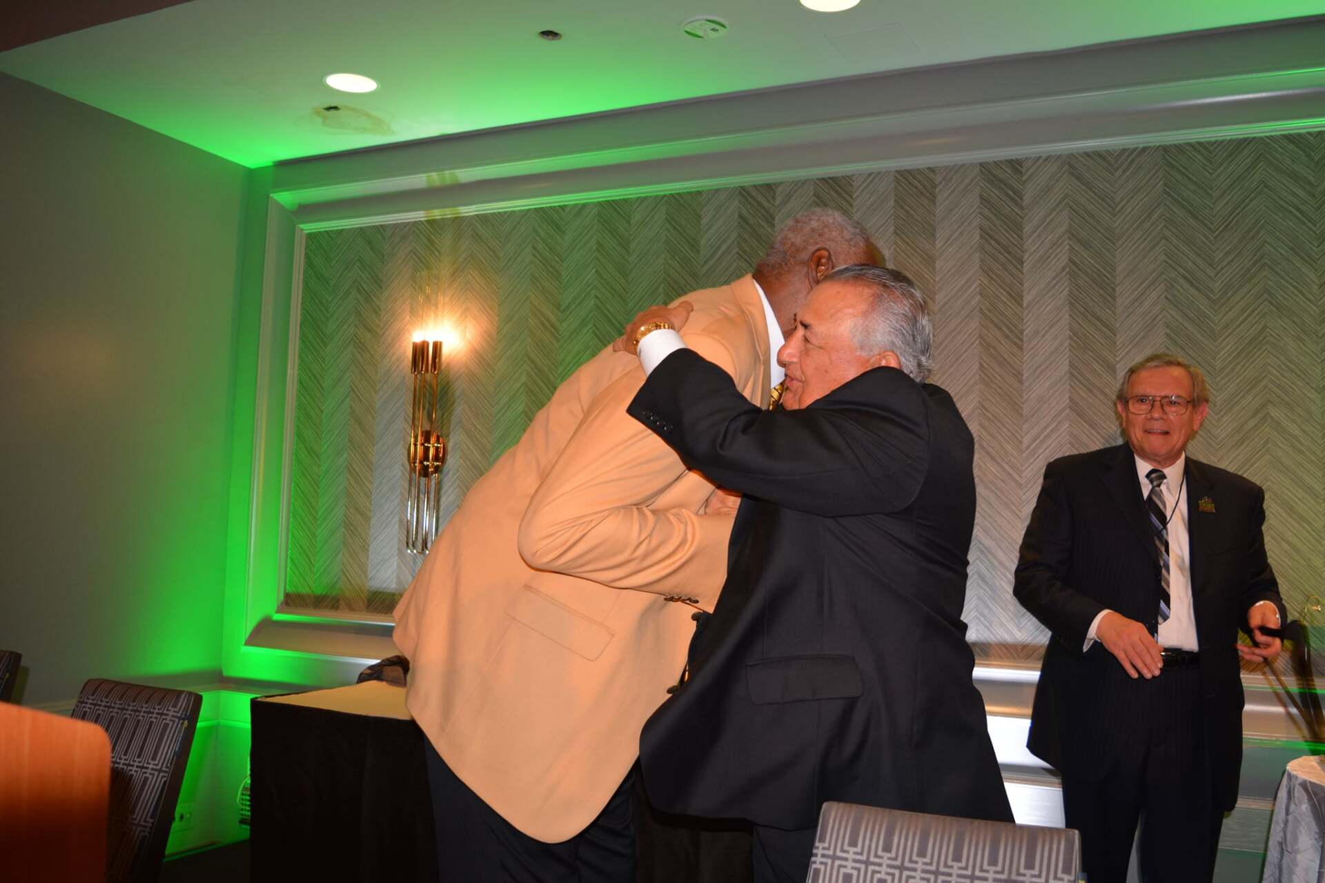 Two men in suits are hugging each other in a room.