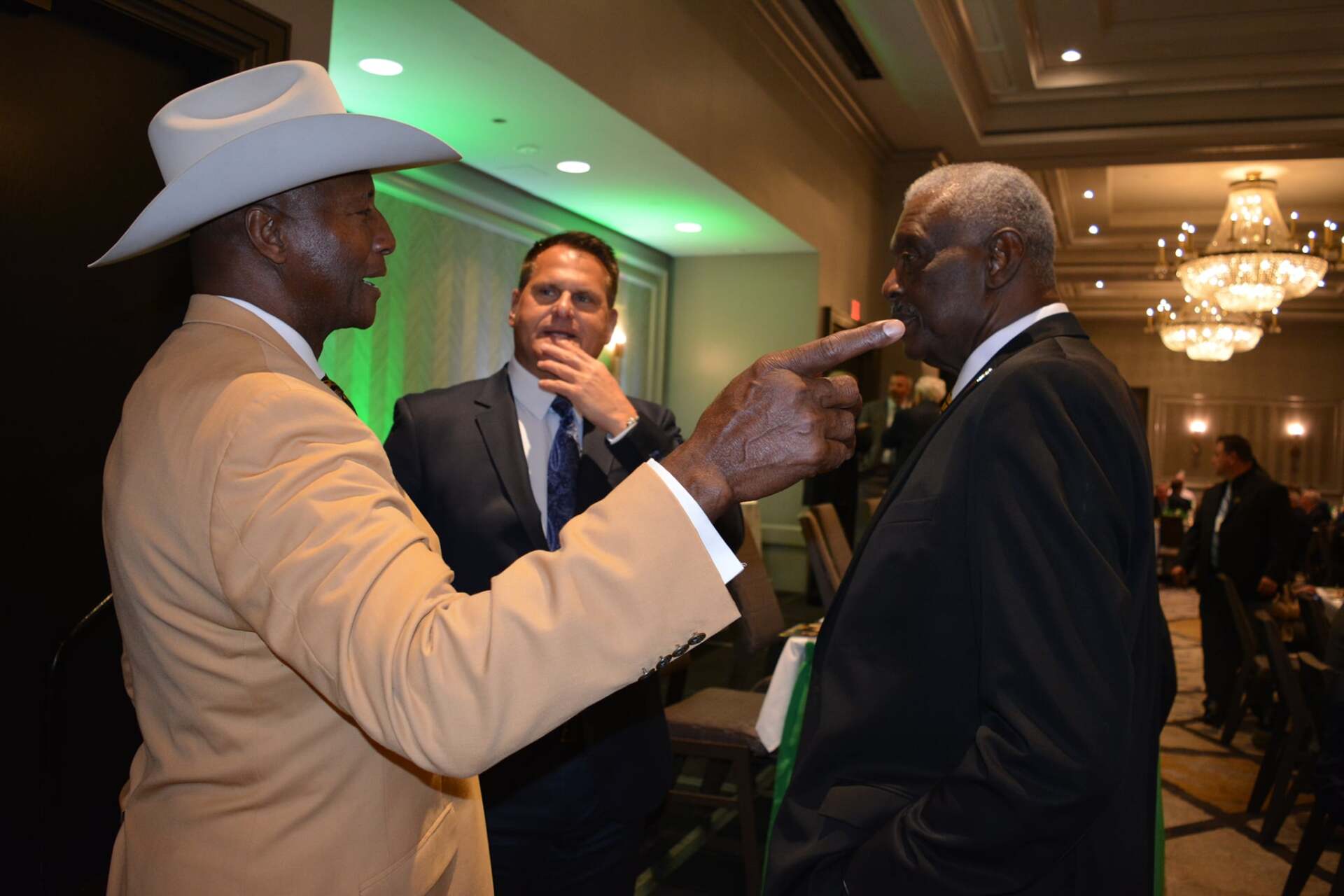 A man in a cowboy hat is pointing at another man in a suit.