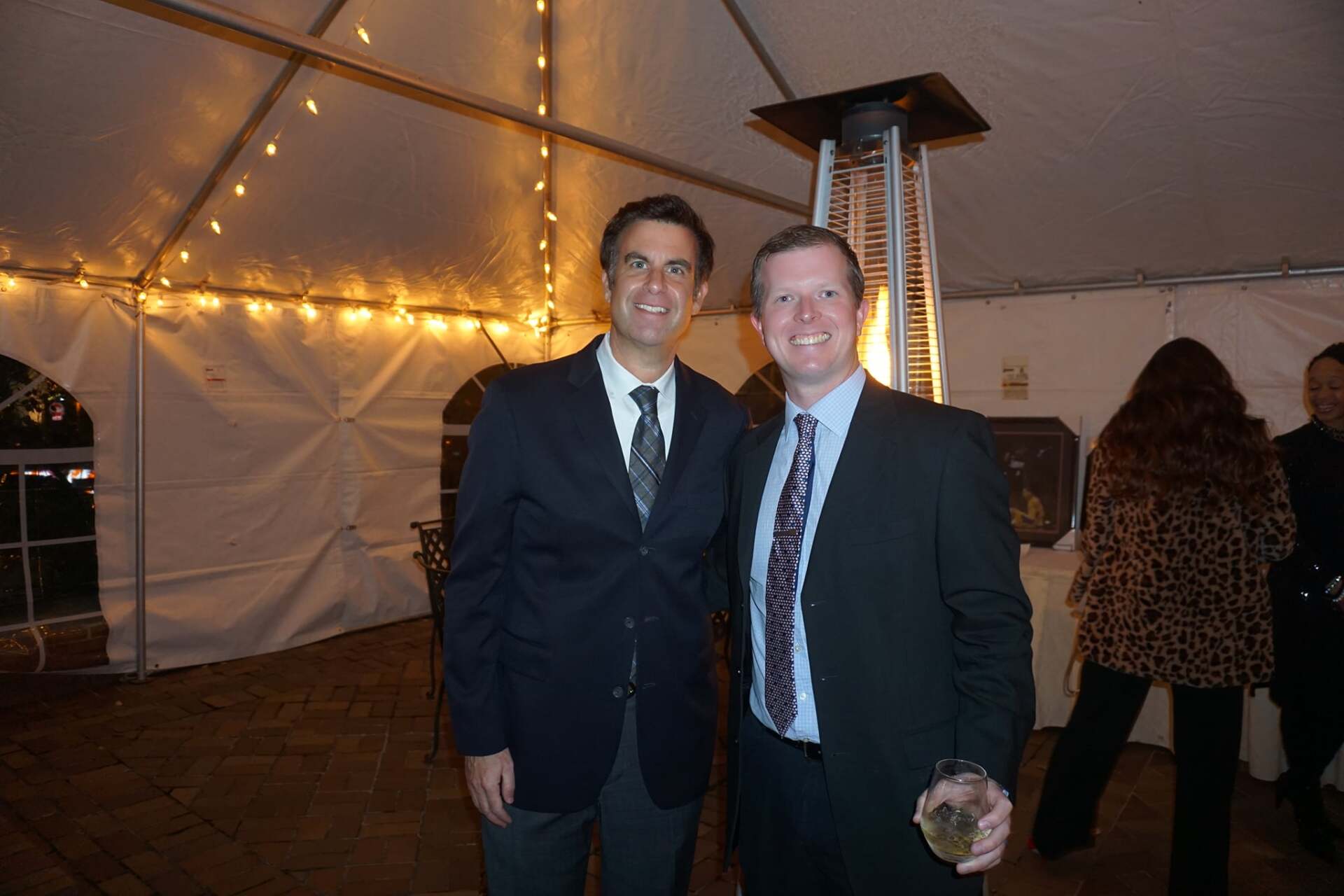Two men in suits and ties are posing for a picture in front of a tent.