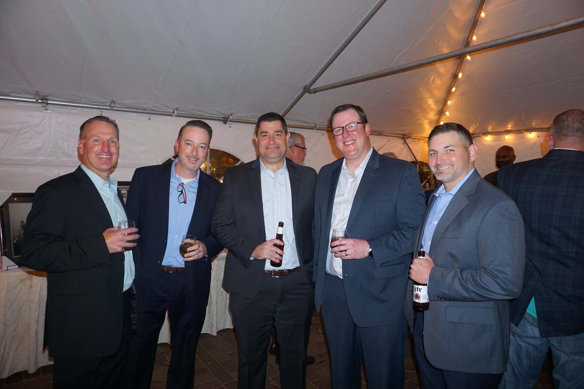 A group of men in suits are posing for a picture under a tent.