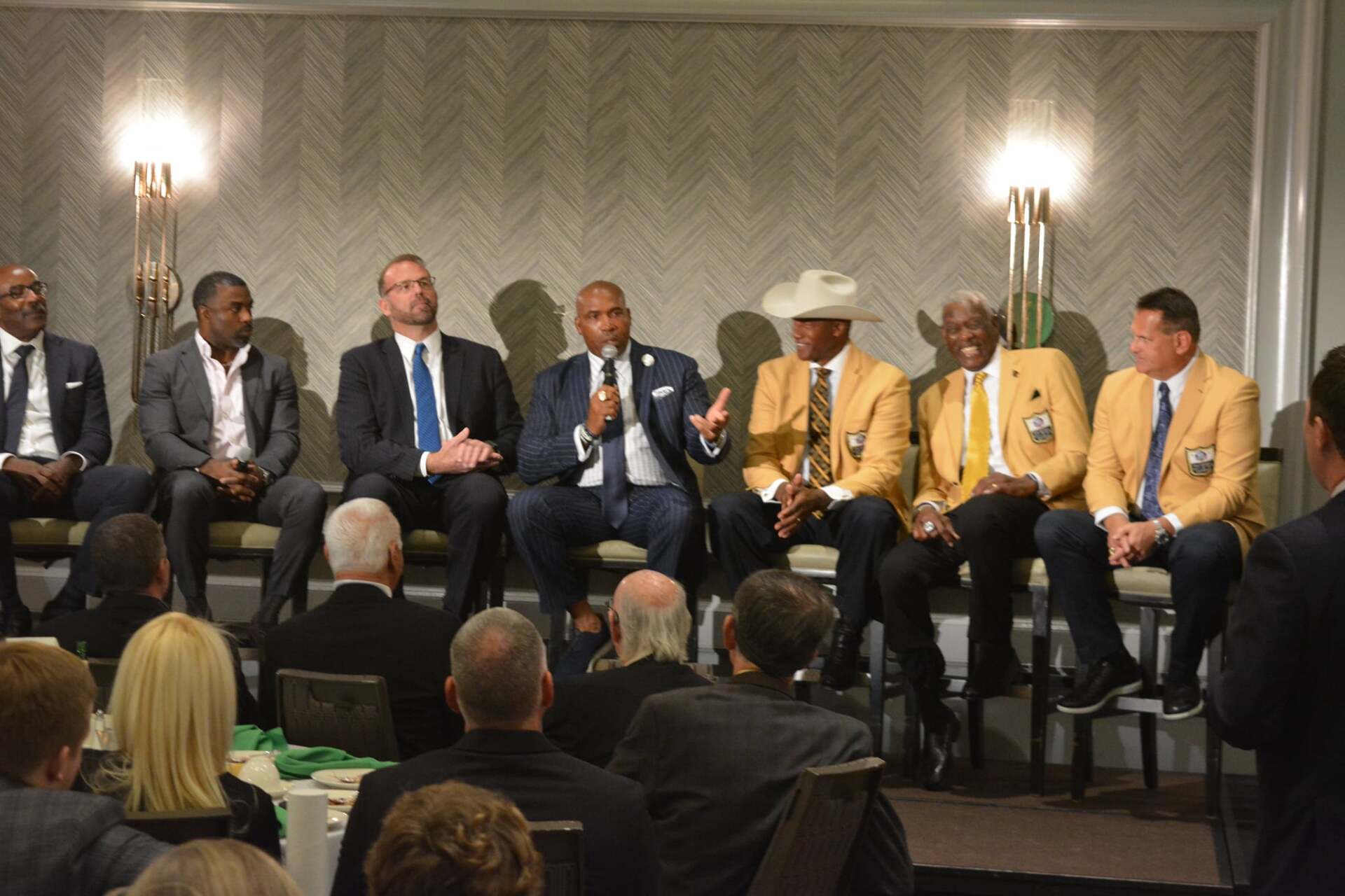 A group of men in suits and ties are sitting in front of a crowd.