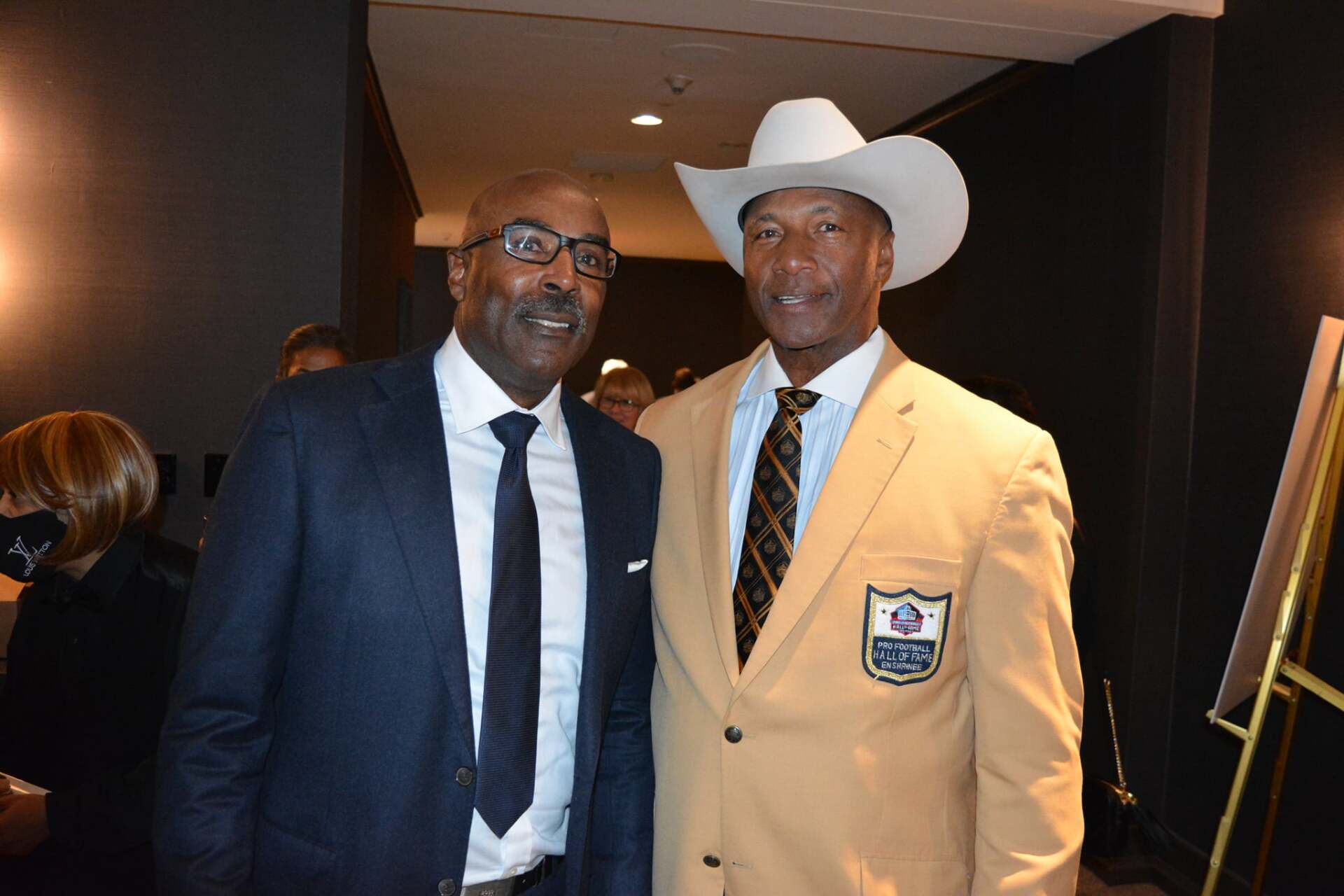 Two men in suits and ties are posing for a picture . one of the men is wearing a cowboy hat.