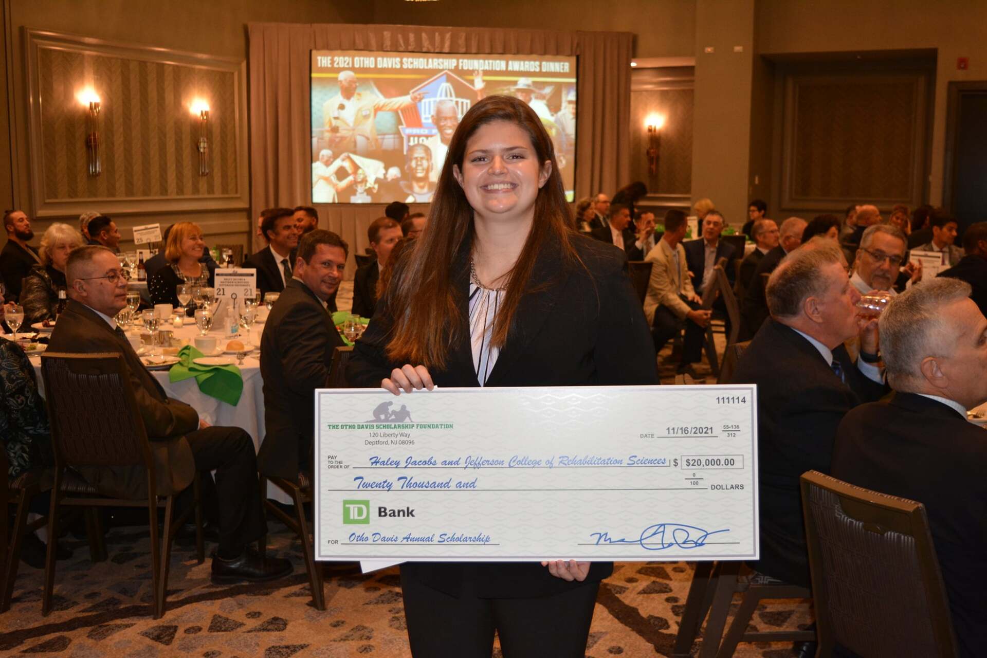 A woman is holding a large check in front of a crowd of people.