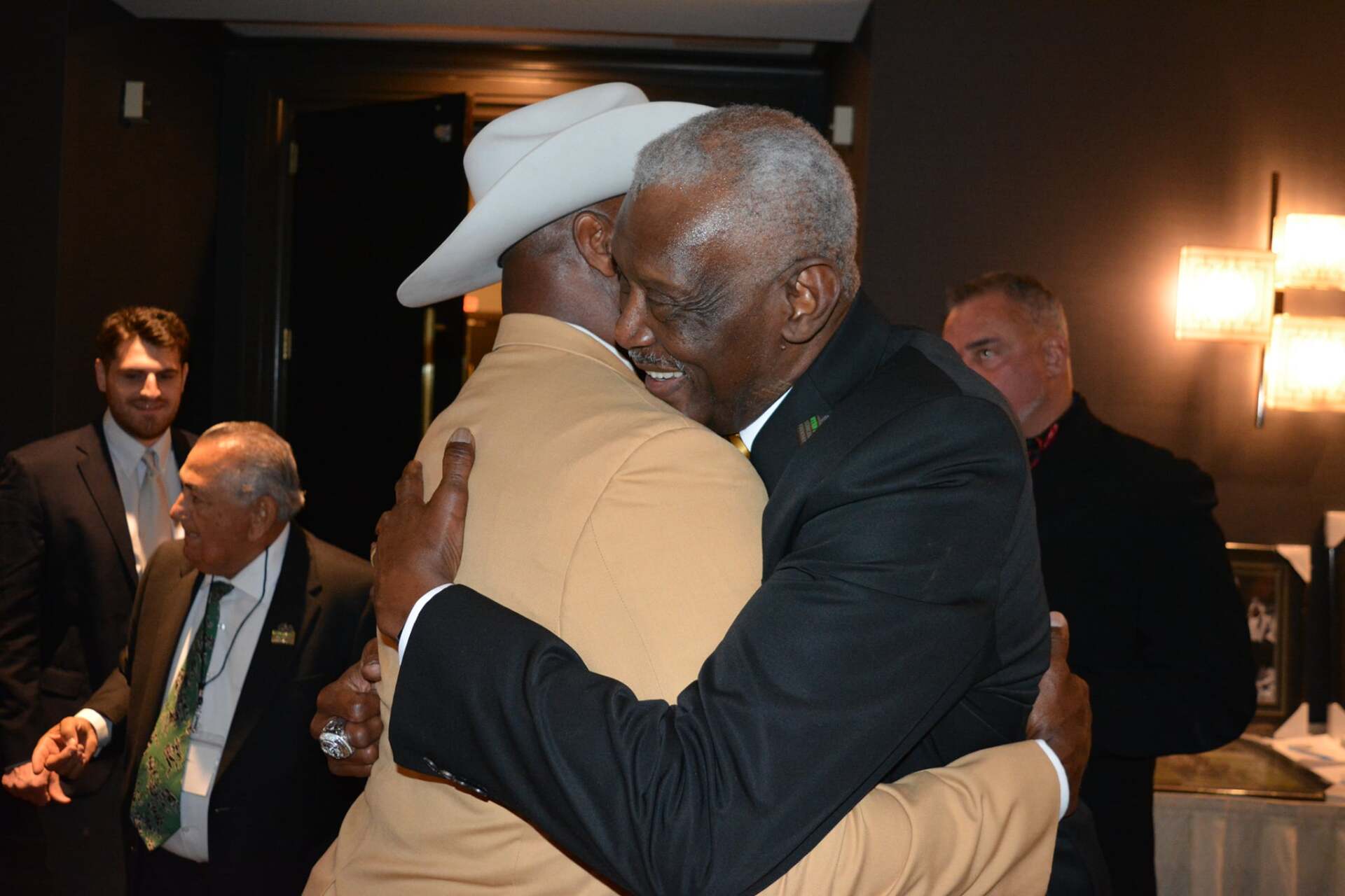 Two men in suits and hats are hugging each other in a room.
