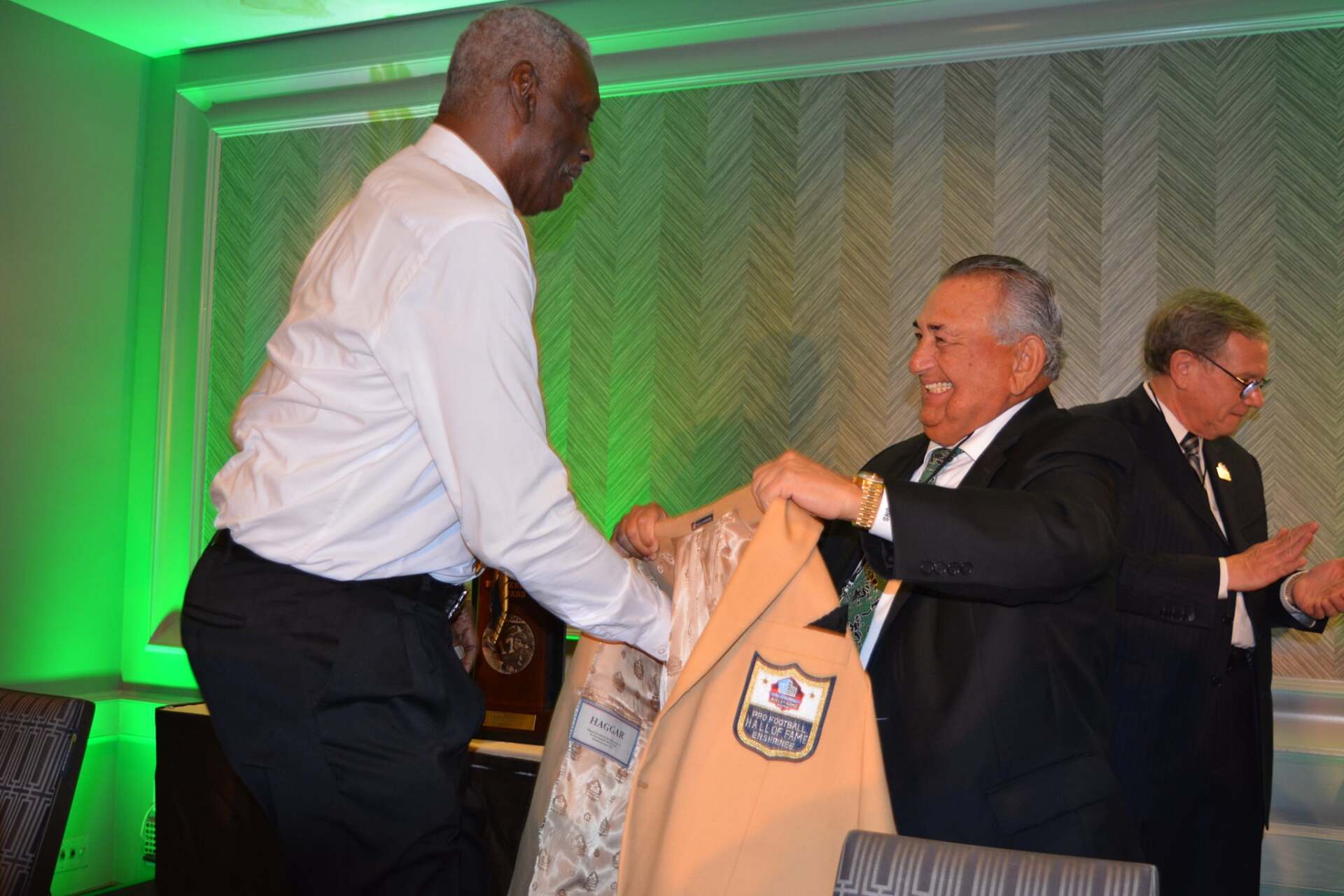 A man in a white shirt is giving a jacket to another man in a suit.