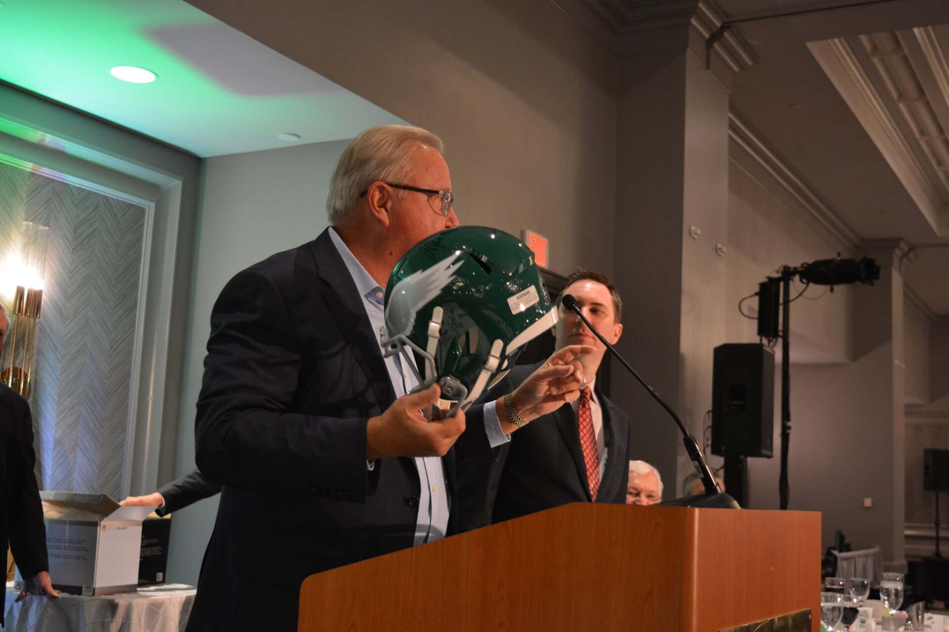 A man is standing at a podium holding a football helmet.