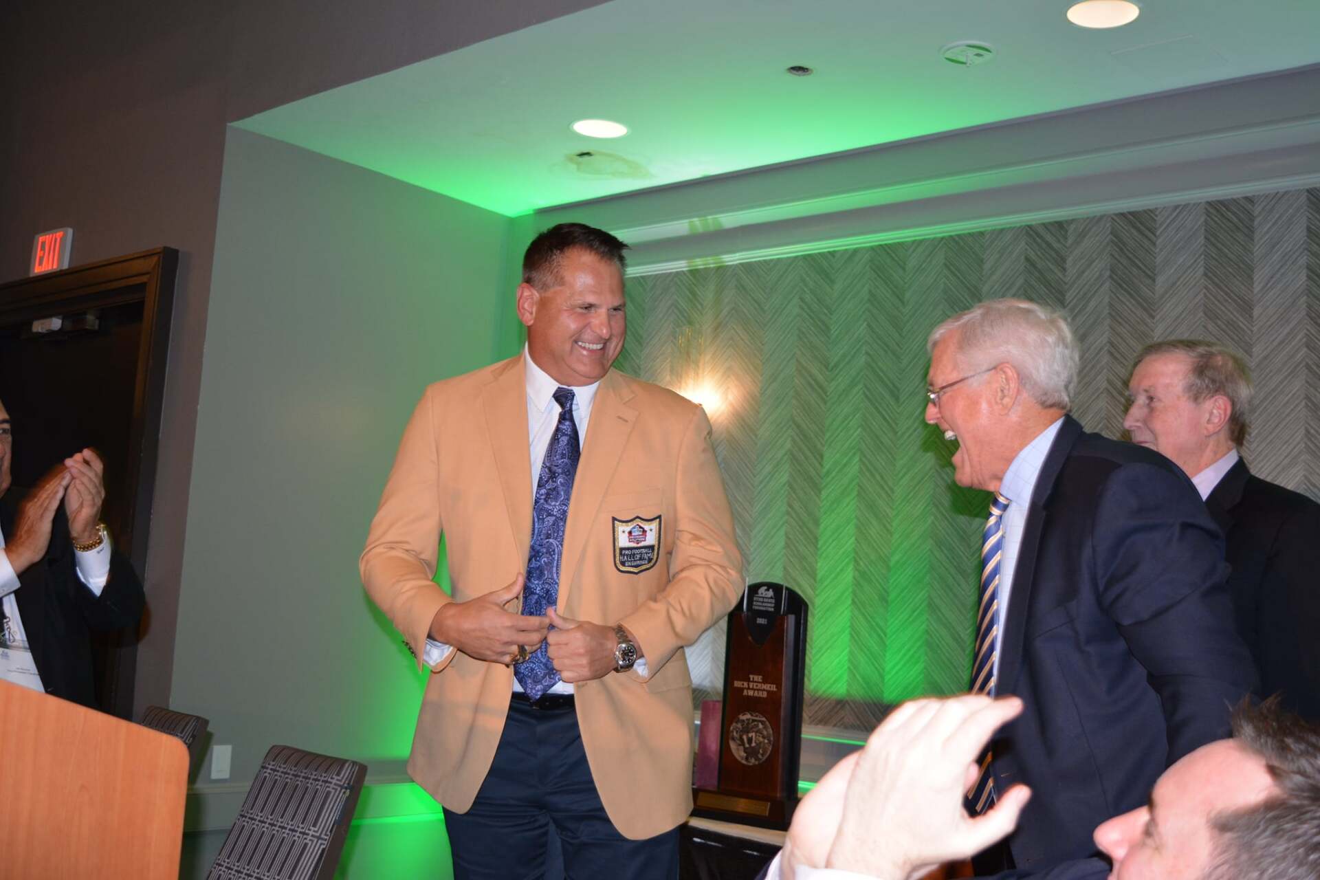 A man in a jacket and tie is standing next to another man in a suit.