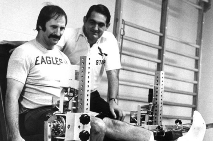 A man wearing an eagles shirt sits next to another man