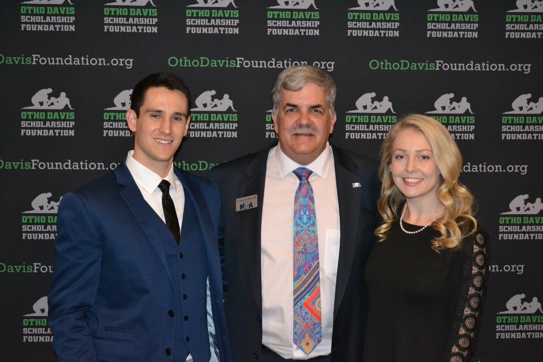 A man in a suit and tie poses with two other people