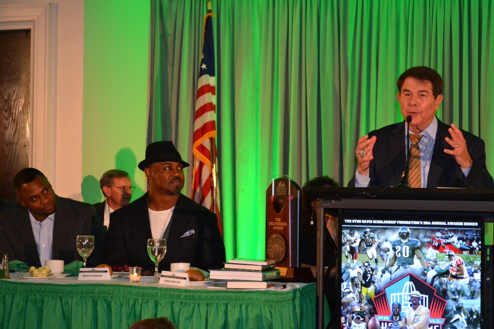 A man is giving a speech at a podium in front of an american flag.