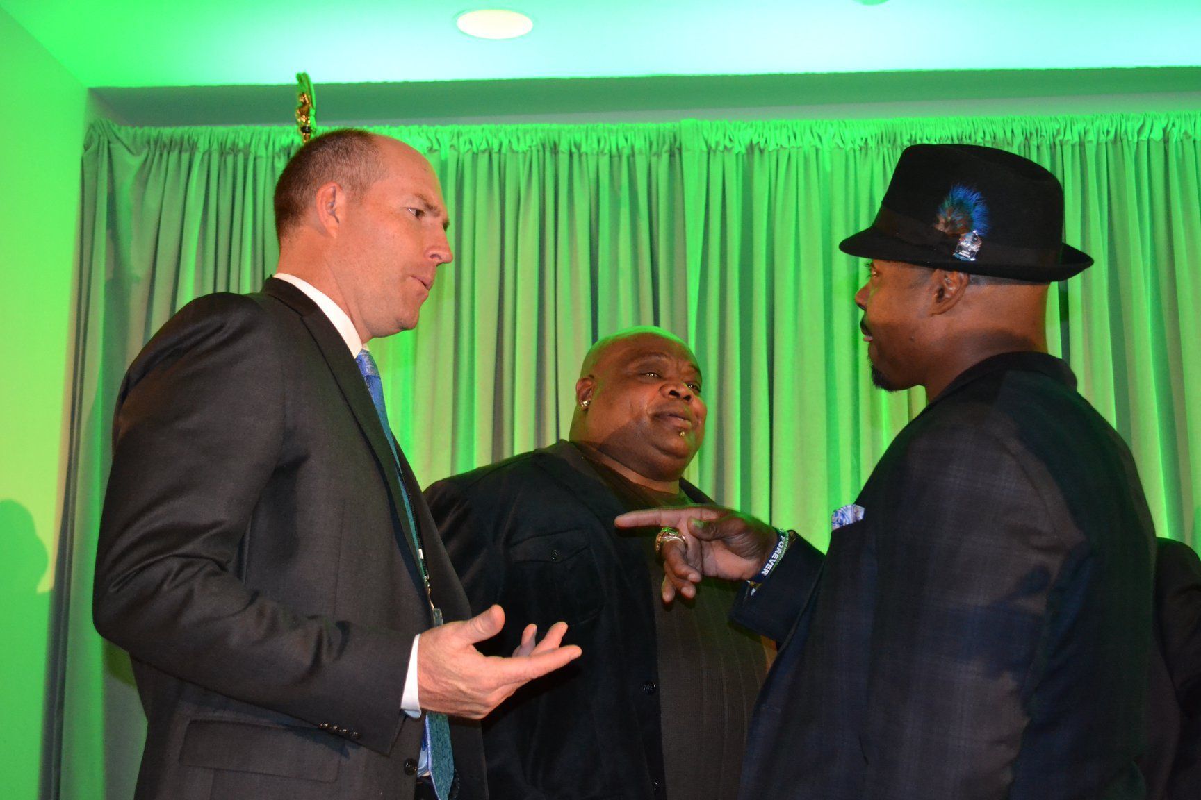 Three men in suits and hats are talking to each other in a room.