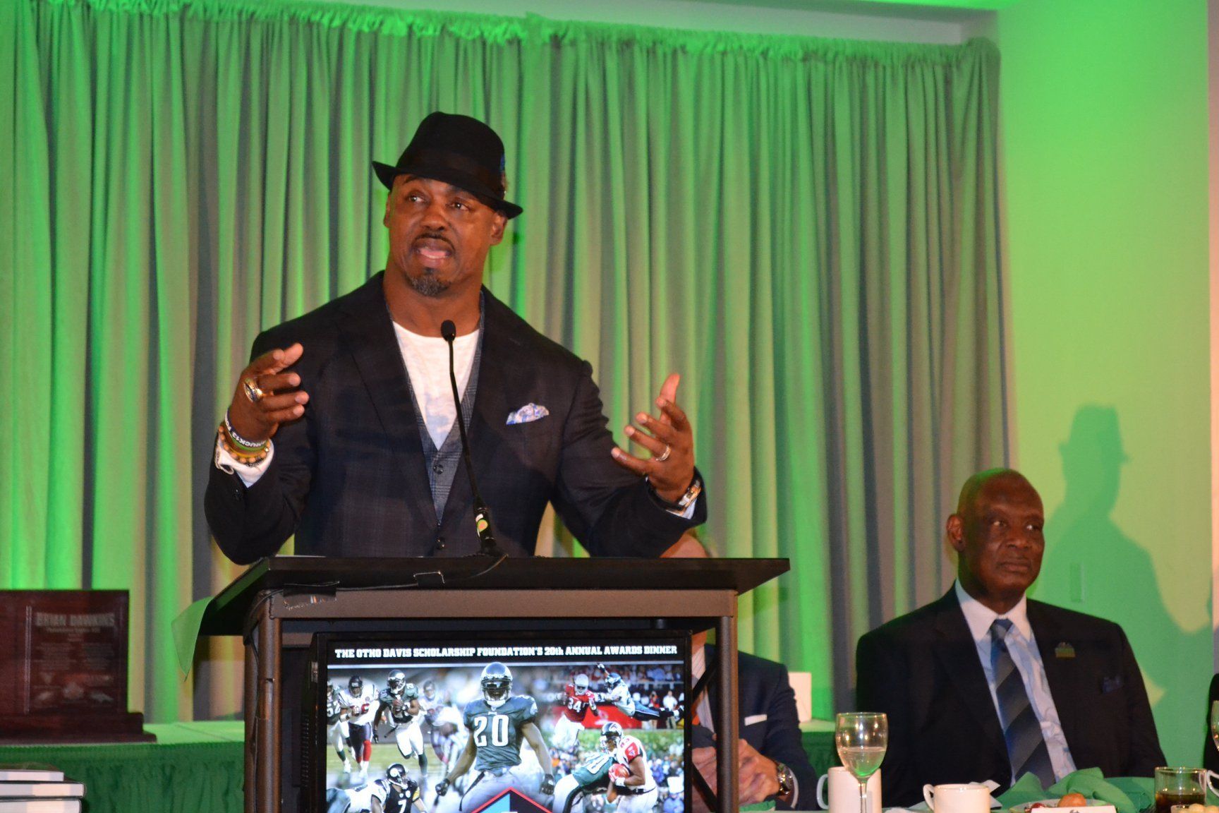 A man in a hat is standing at a podium giving a speech.