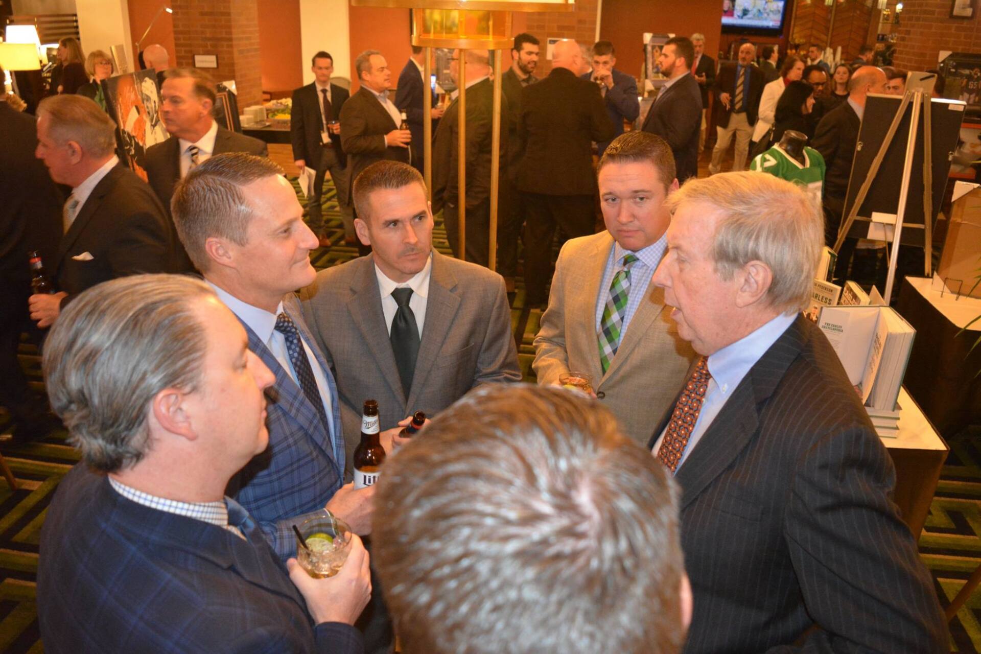 A group of men in suits and ties are standing around a table talking.