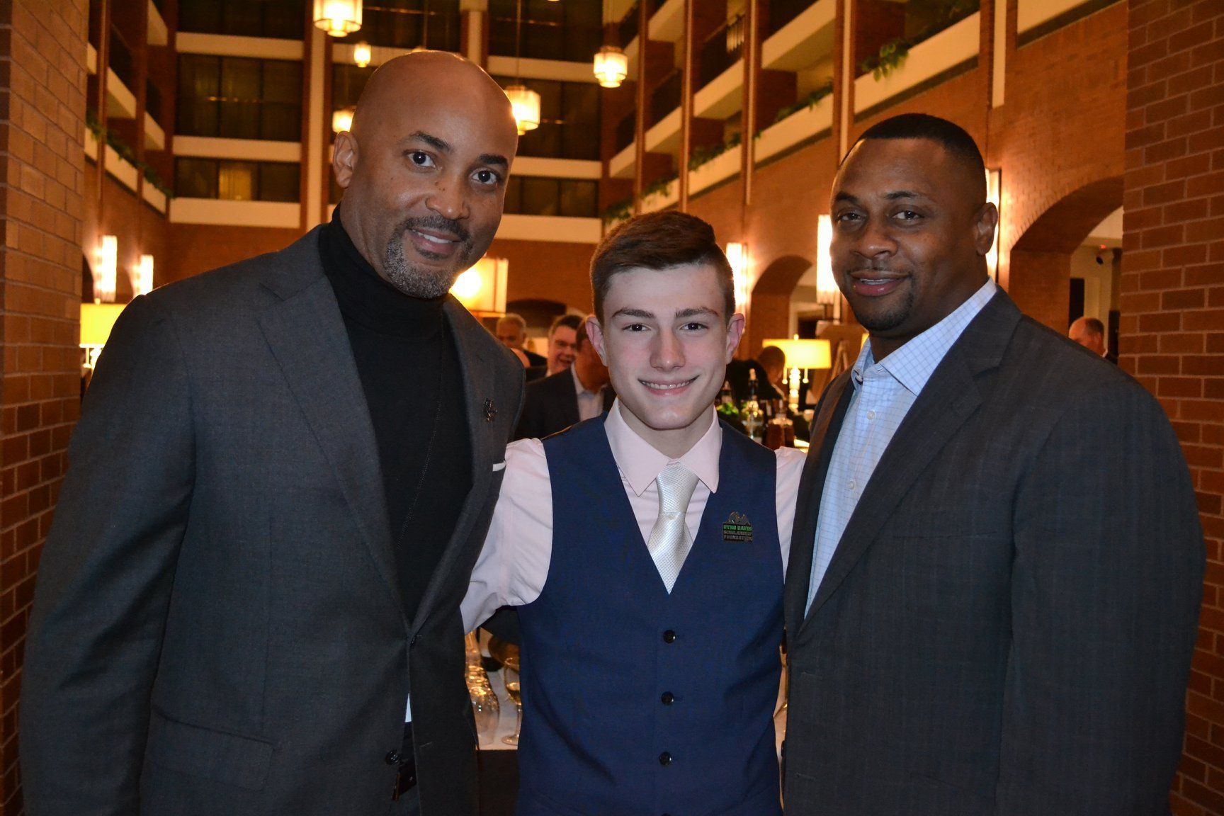 Three men in suits are posing for a picture with a boy in a vest.