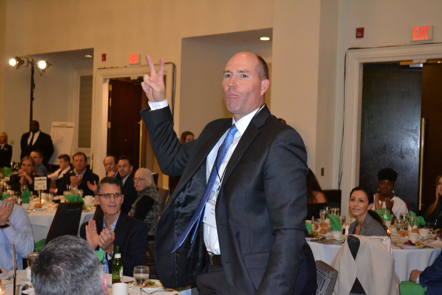 A man in a suit and tie is standing in front of a group of people at a dinner table.