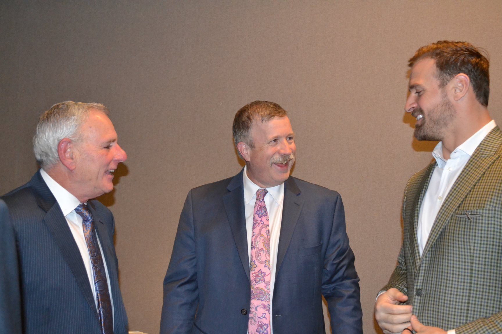 Three men in suits and ties are standing next to each other and talking.