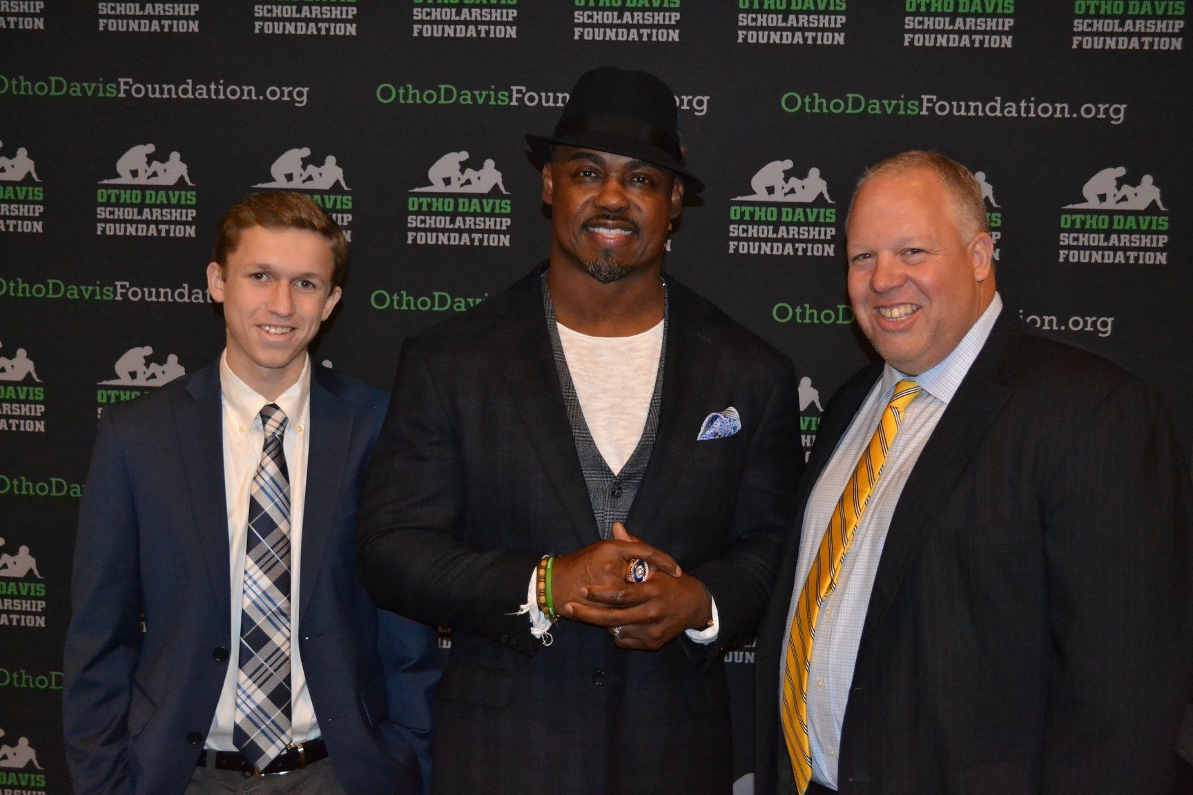 Three men are posing for a picture in front of a wall that says otto davis foundation