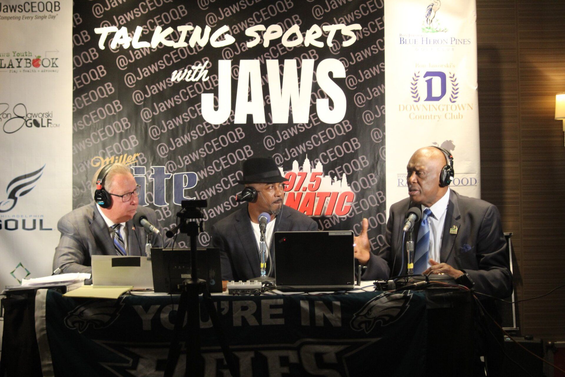 A group of men are sitting in front of a sign that says talking sports jaws