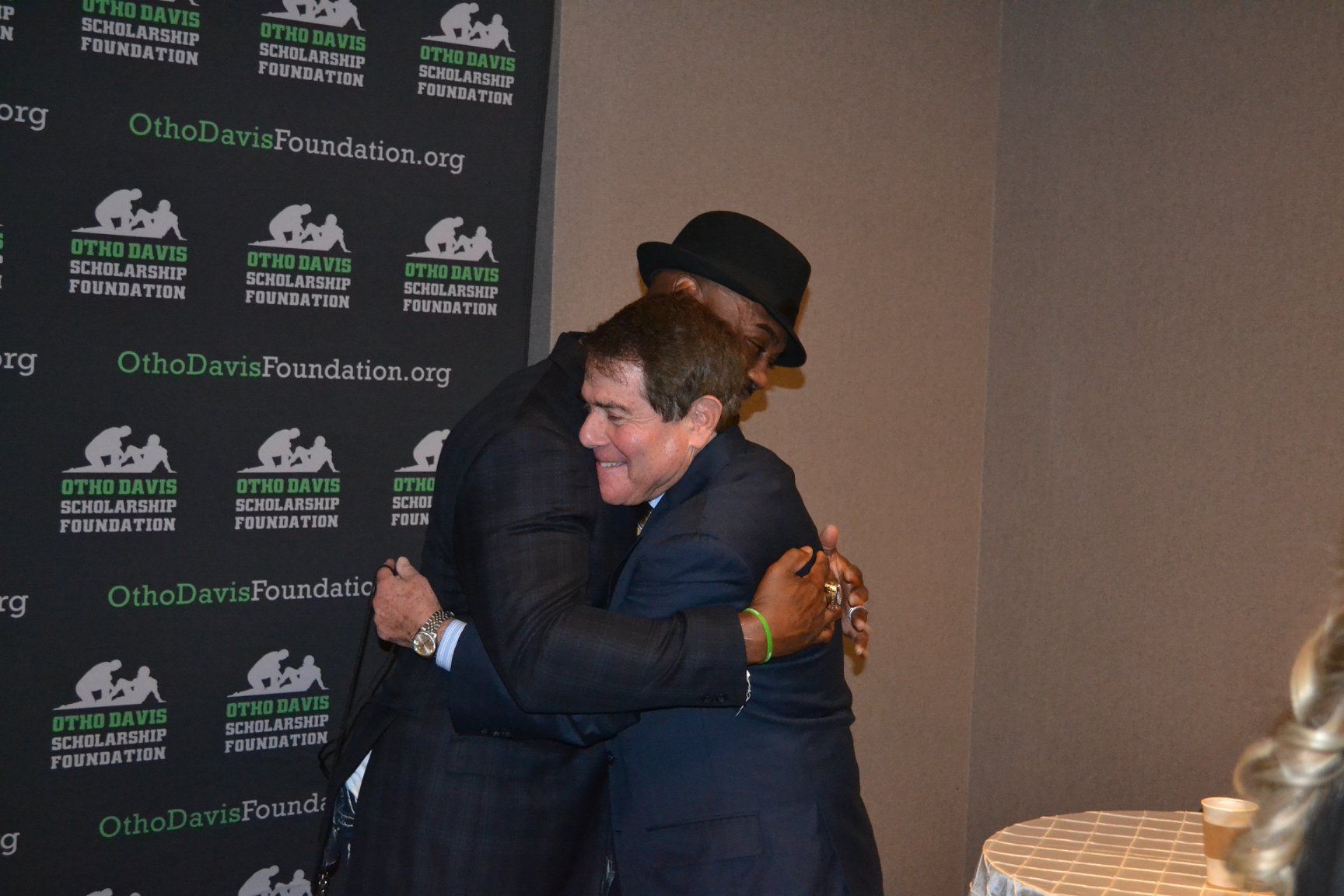 A man in a suit and hat is hugging another man