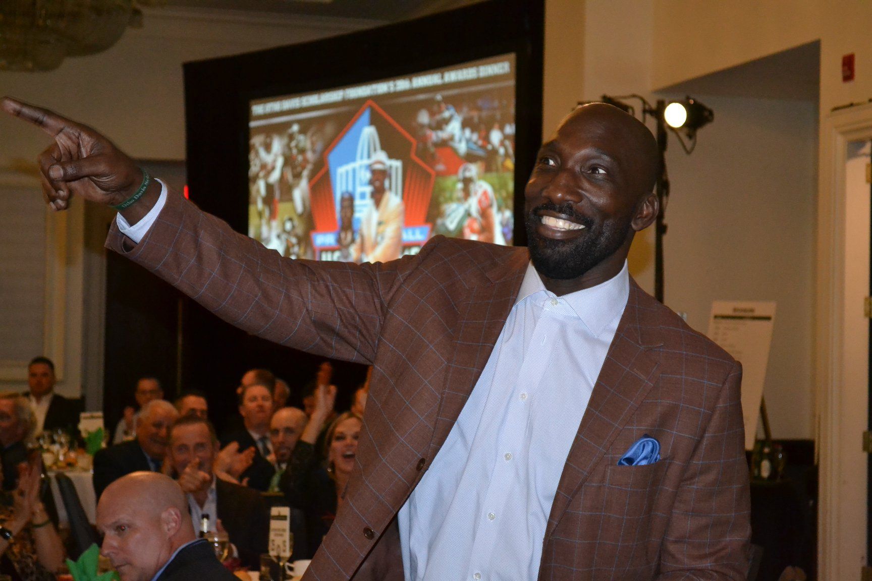 A man in a brown suit is pointing at something in front of a crowd.