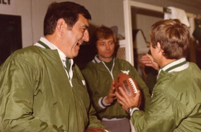 A man in a green jacket is holding a football
