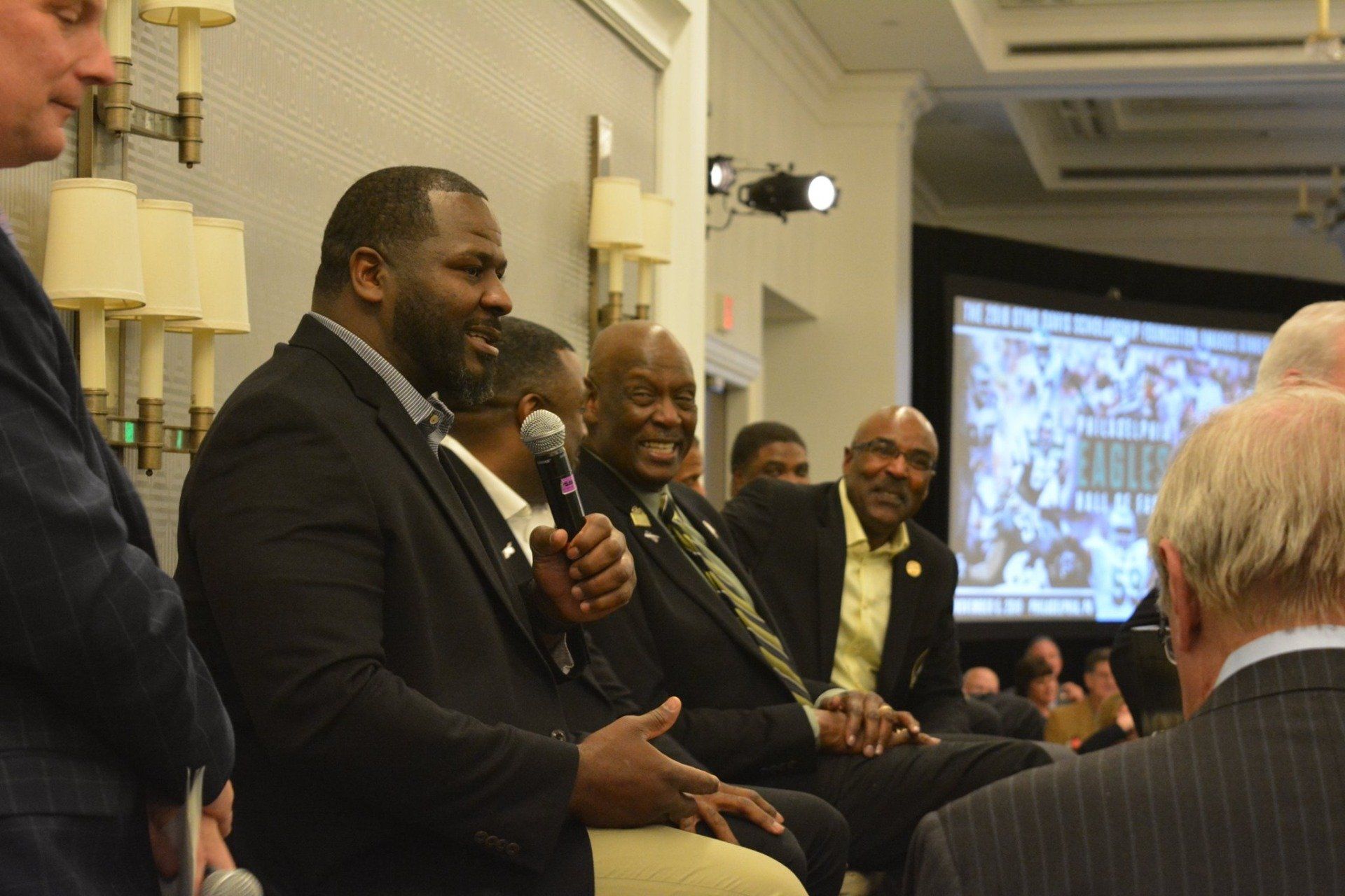 A man is holding a microphone and talking to a group of people.
