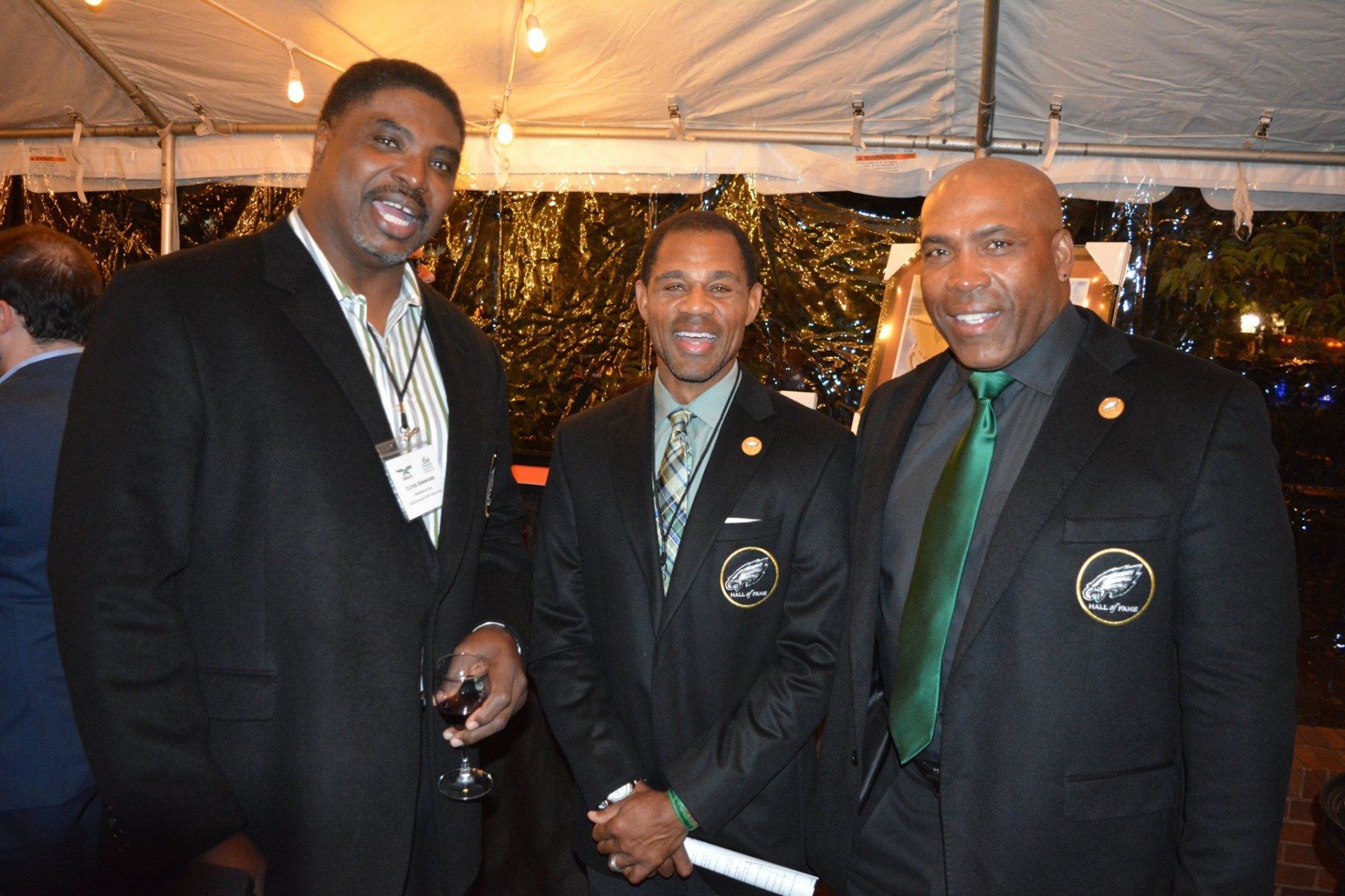 Three men in suits and ties are posing for a picture under a tent.
