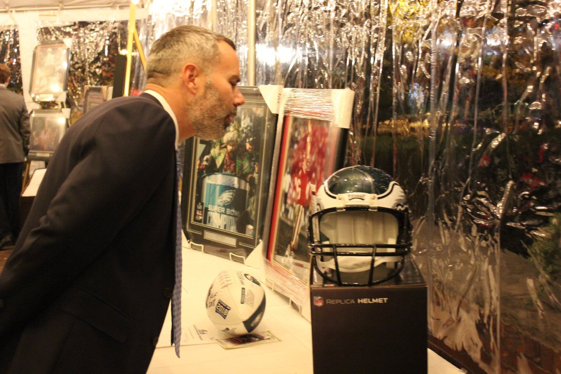 A man in a suit and tie is looking at a football helmet