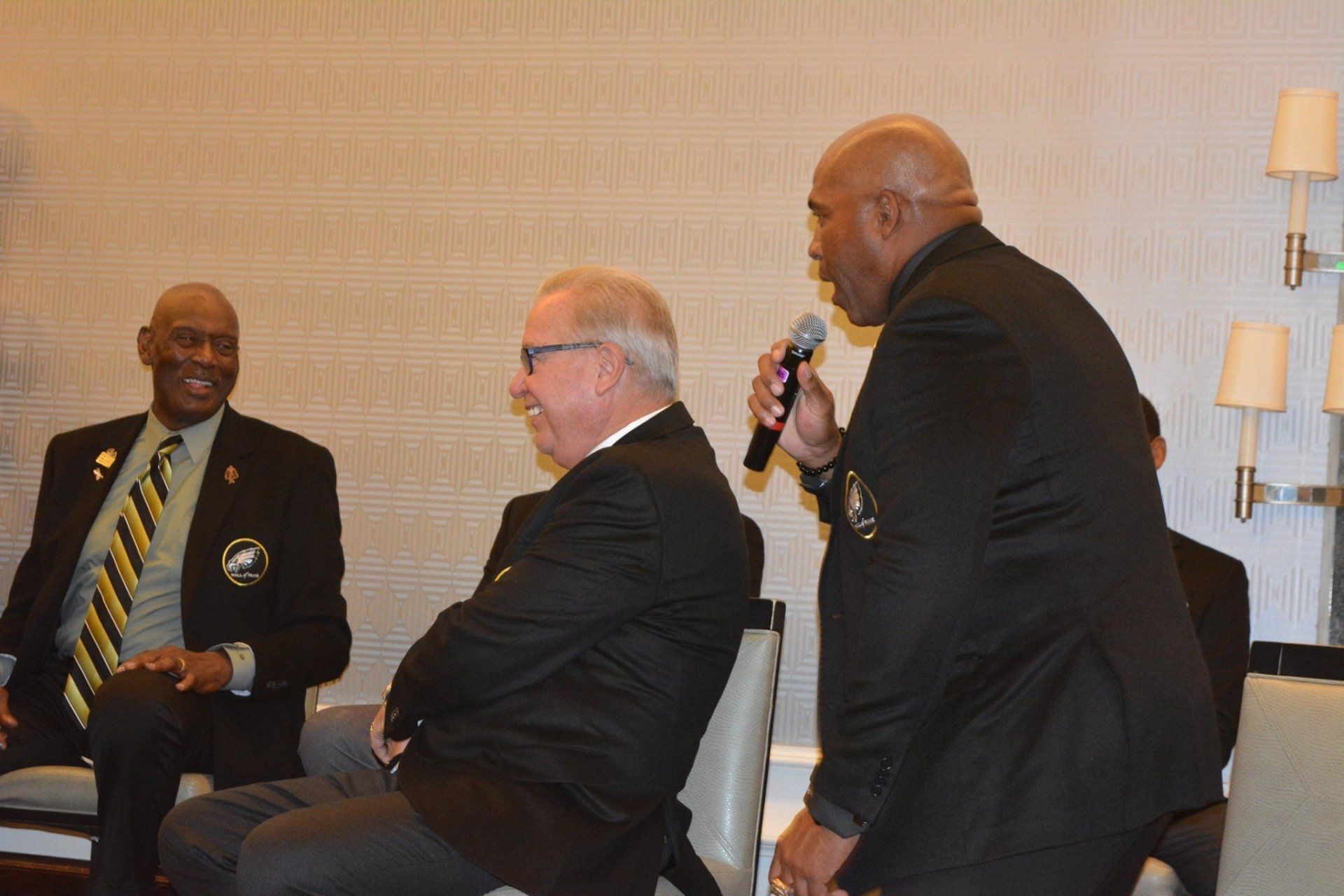 A group of men are sitting in chairs and one man is holding a microphone.