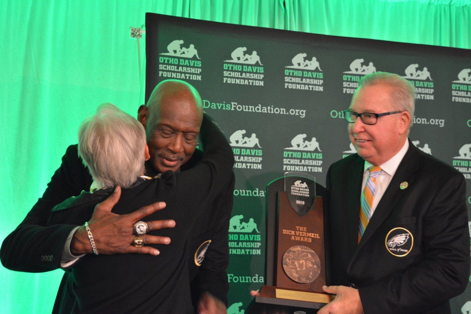 A man is hugging another man while holding a trophy.