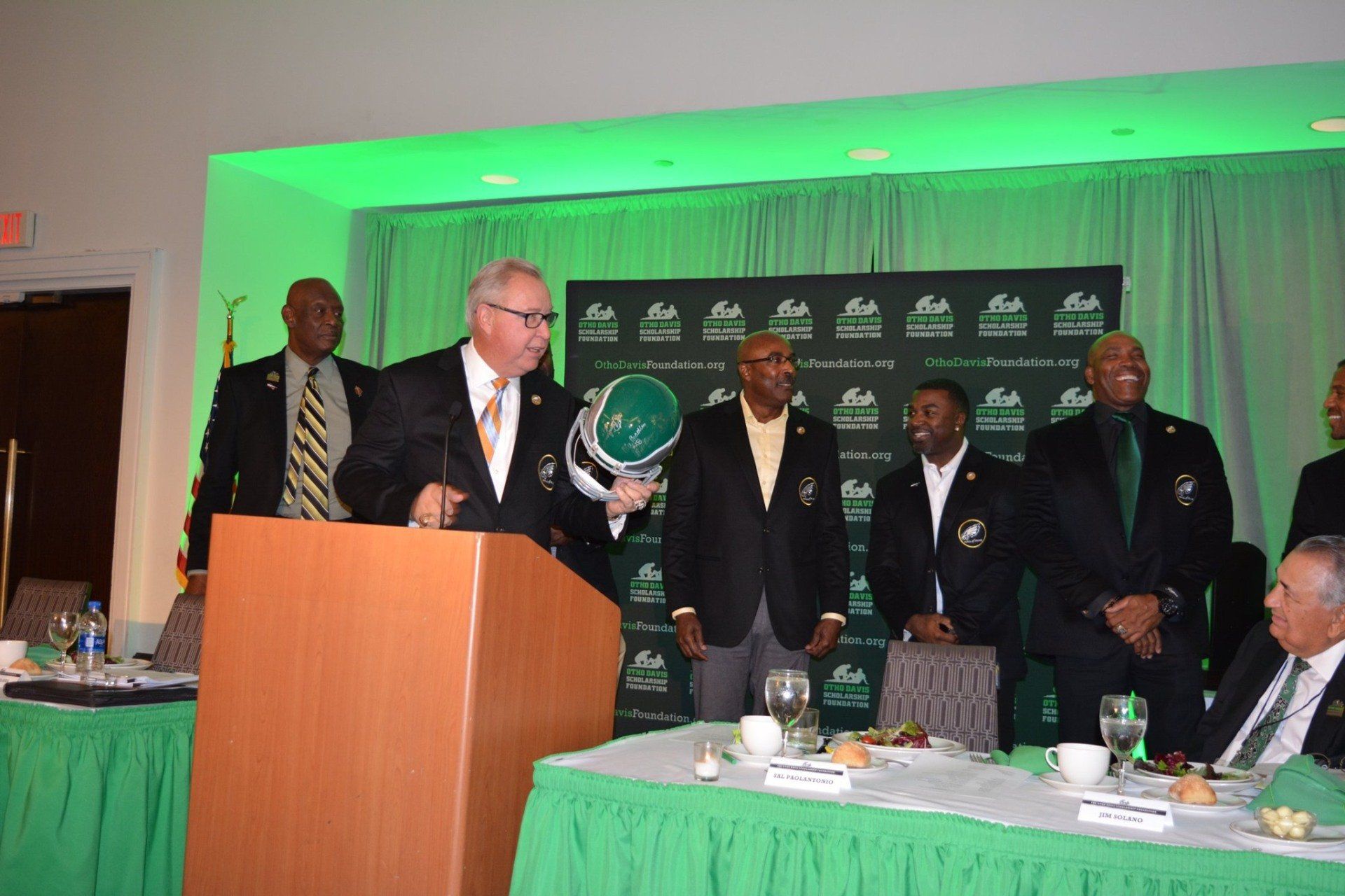 A man is giving a speech at a podium in front of a group of men.