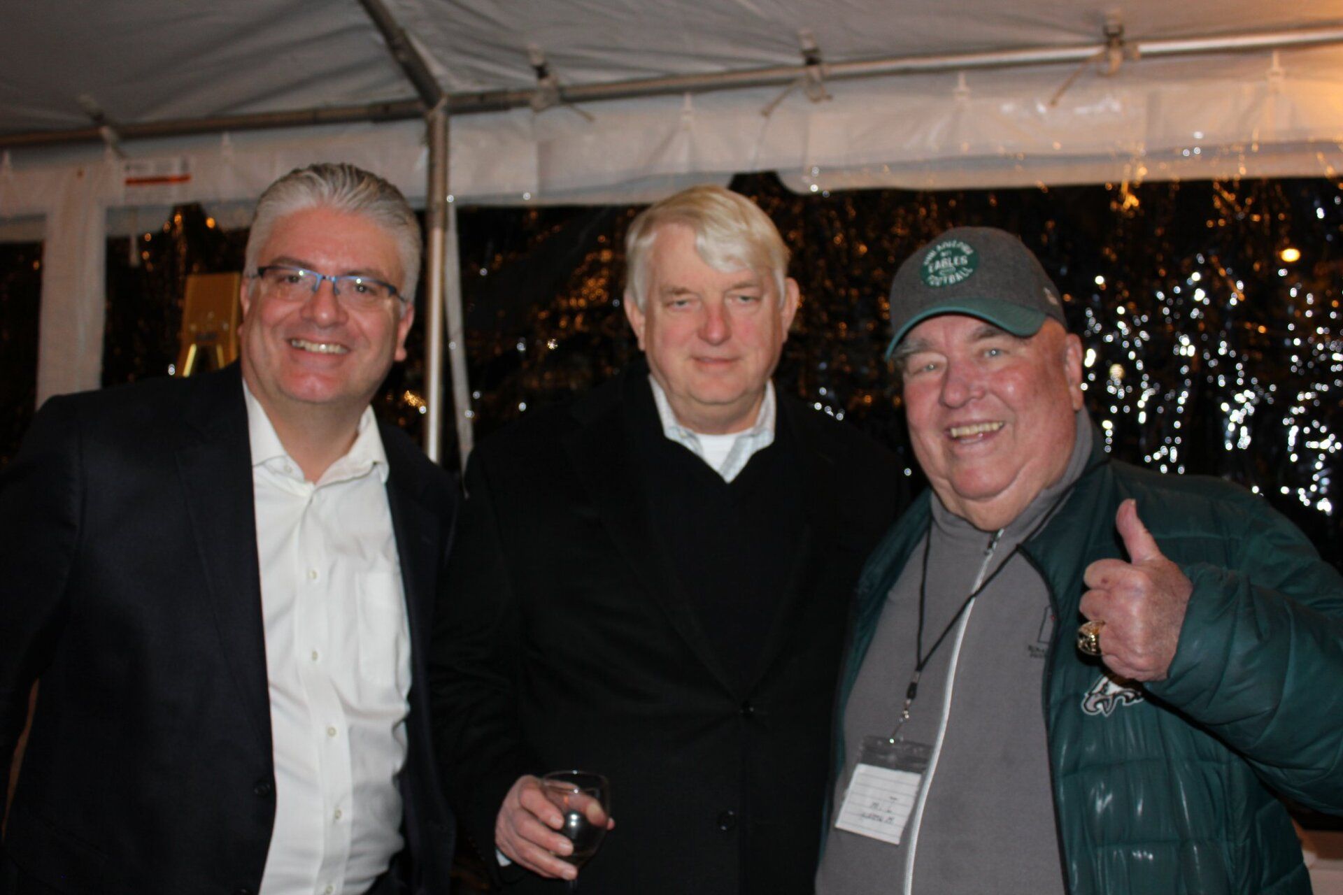 Three men are posing for a picture and one of them is giving a thumbs up.
