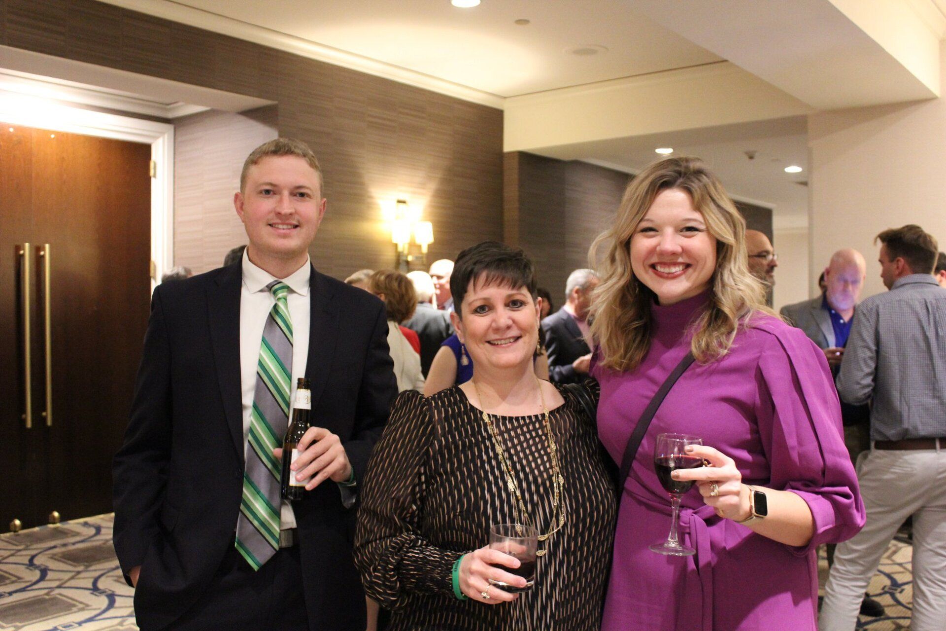 A man in a suit and tie is standing next to two women holding wine glasses.