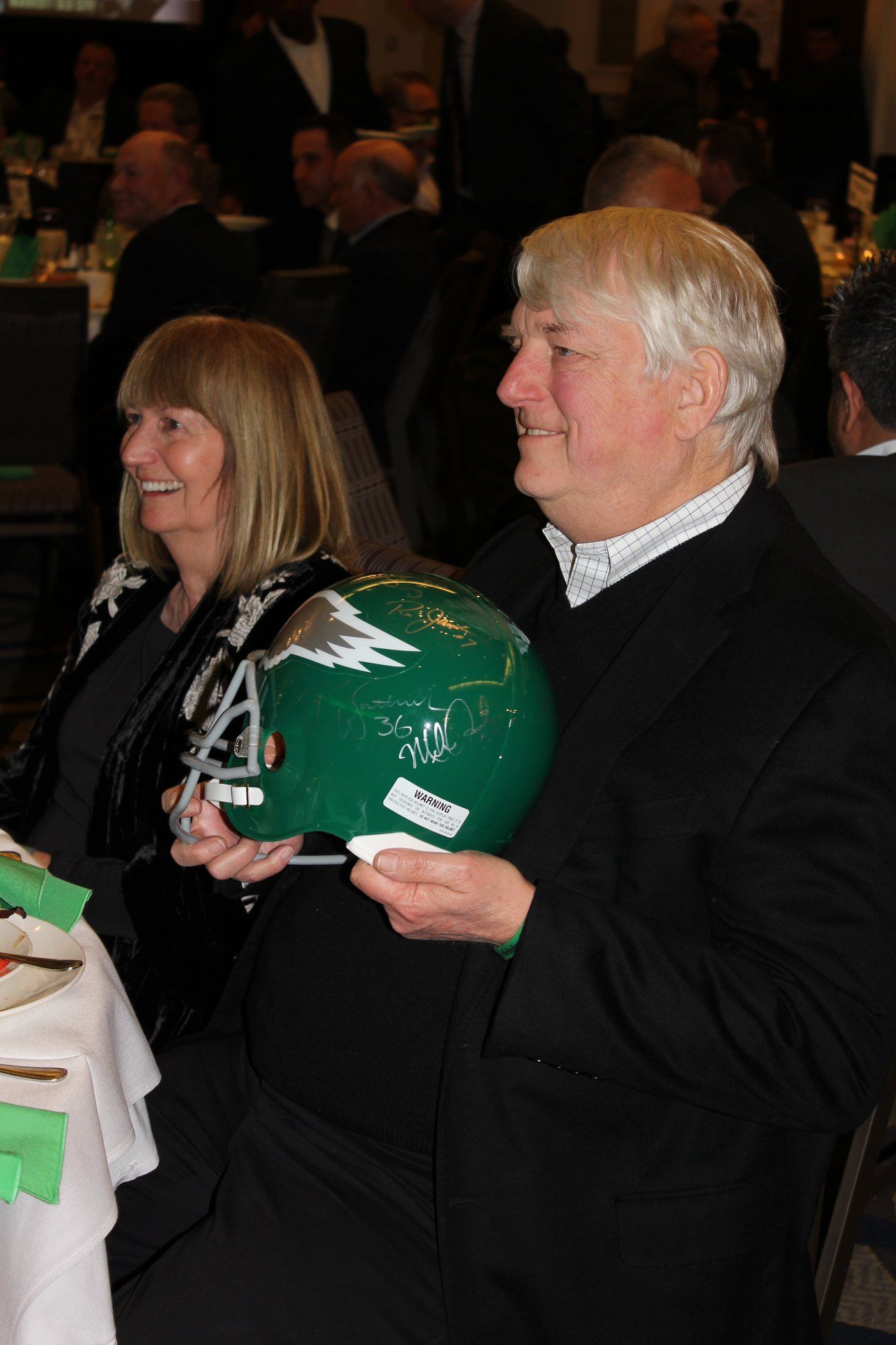 A man and a woman are sitting at a table holding a green helmet.