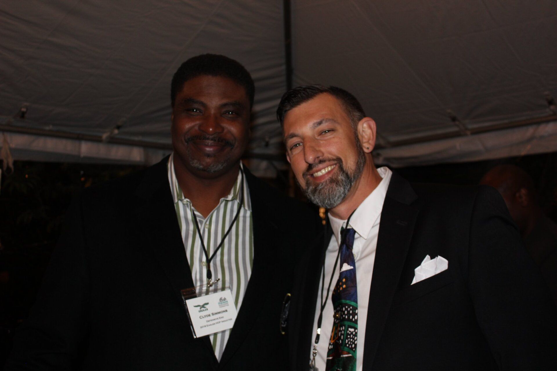 Two men posing for a picture with one wearing a name tag