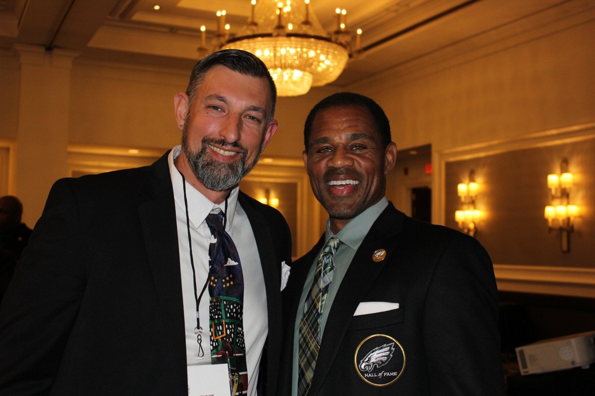 Two men are posing for a picture in a room with a chandelier in the background.