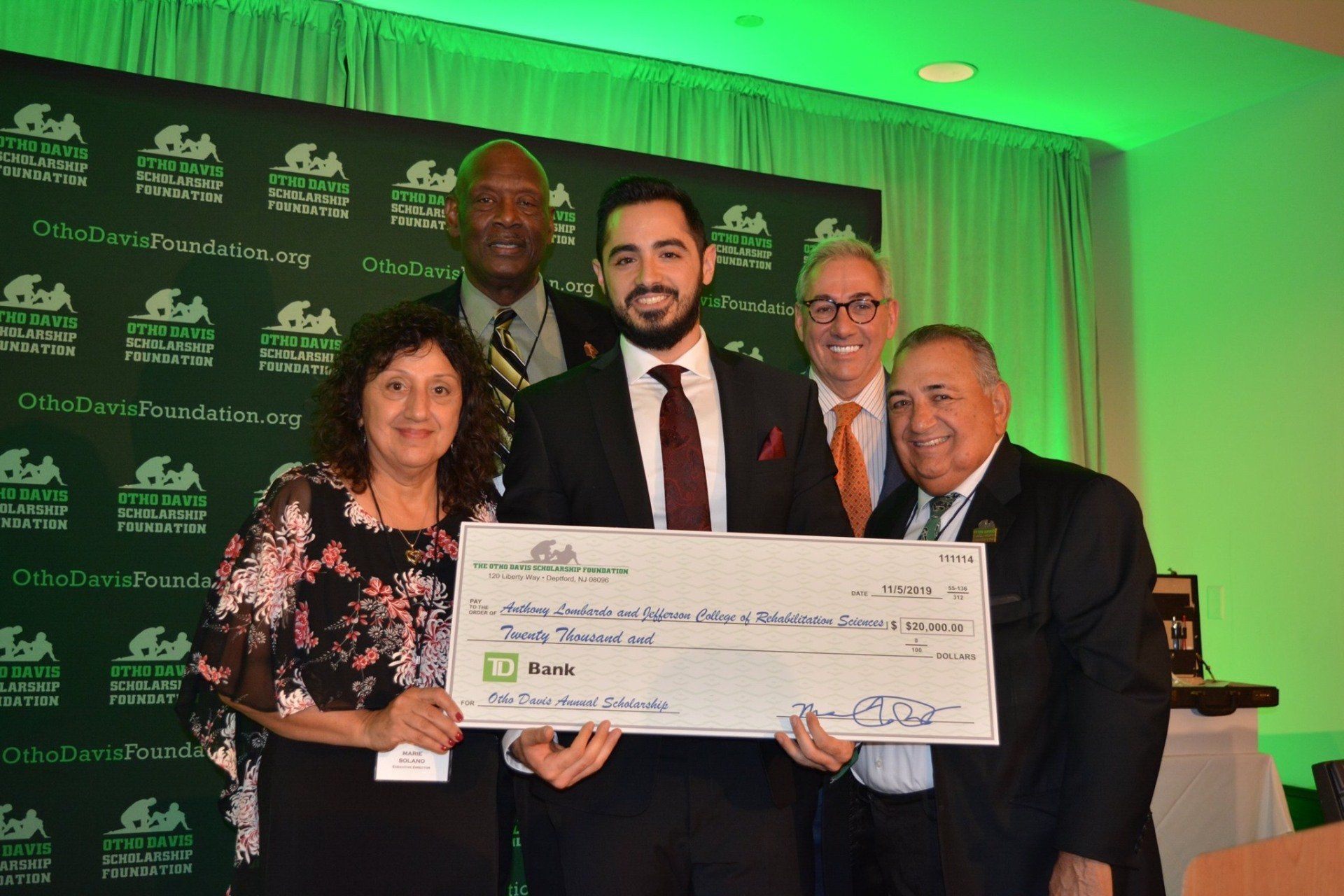 A group of people are standing around a man holding a large check.