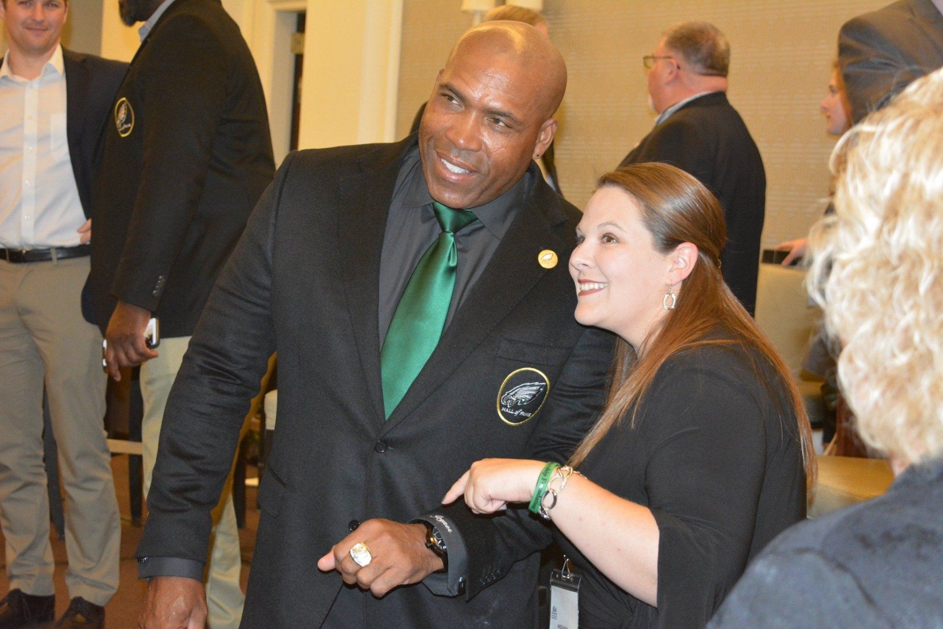 A man in a black suit and green tie is talking to a woman in a black shirt.