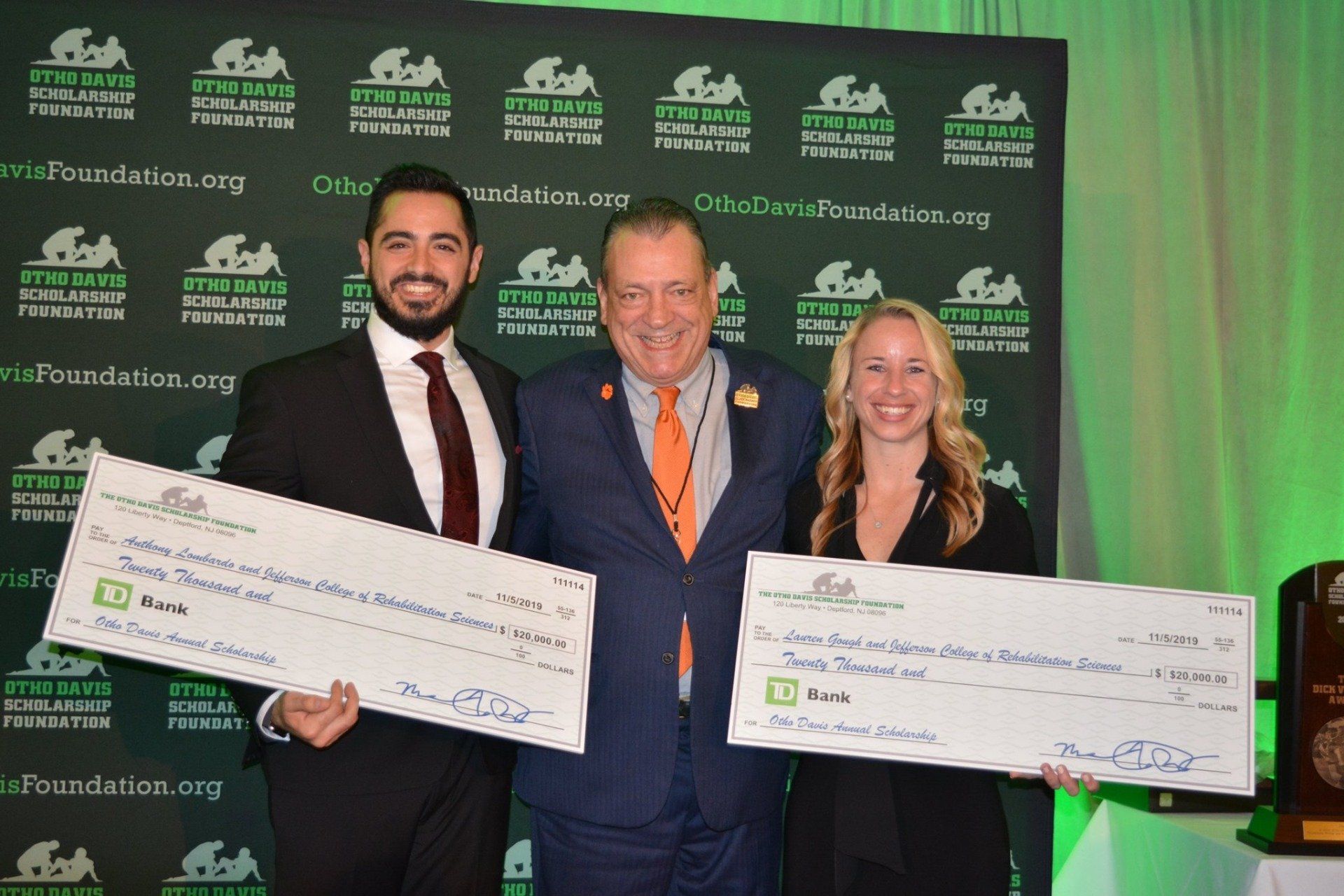 A man and two women are holding checks in front of a green wall.