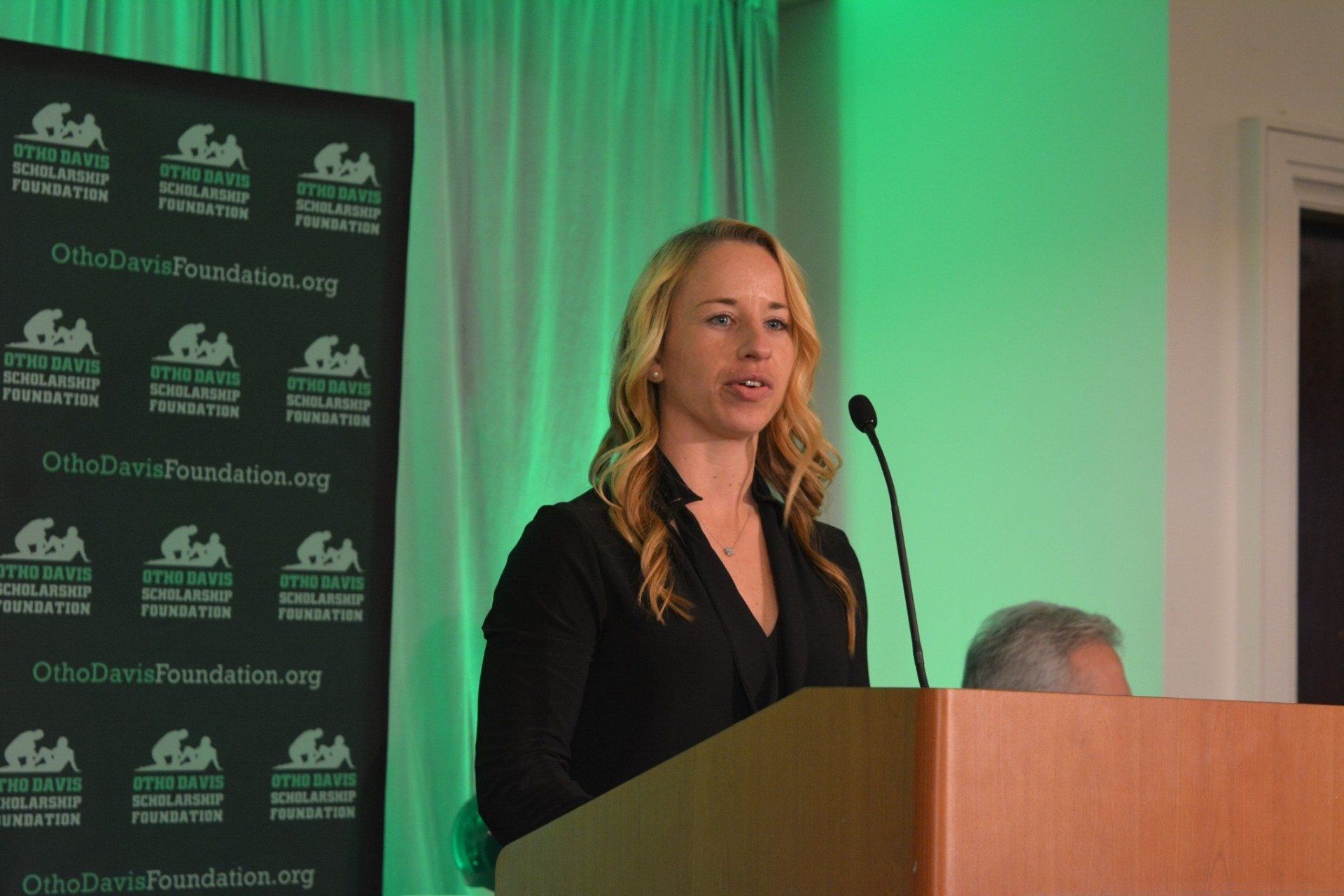 A woman is standing at a podium with a microphone in front of a sign that says ' ocb '