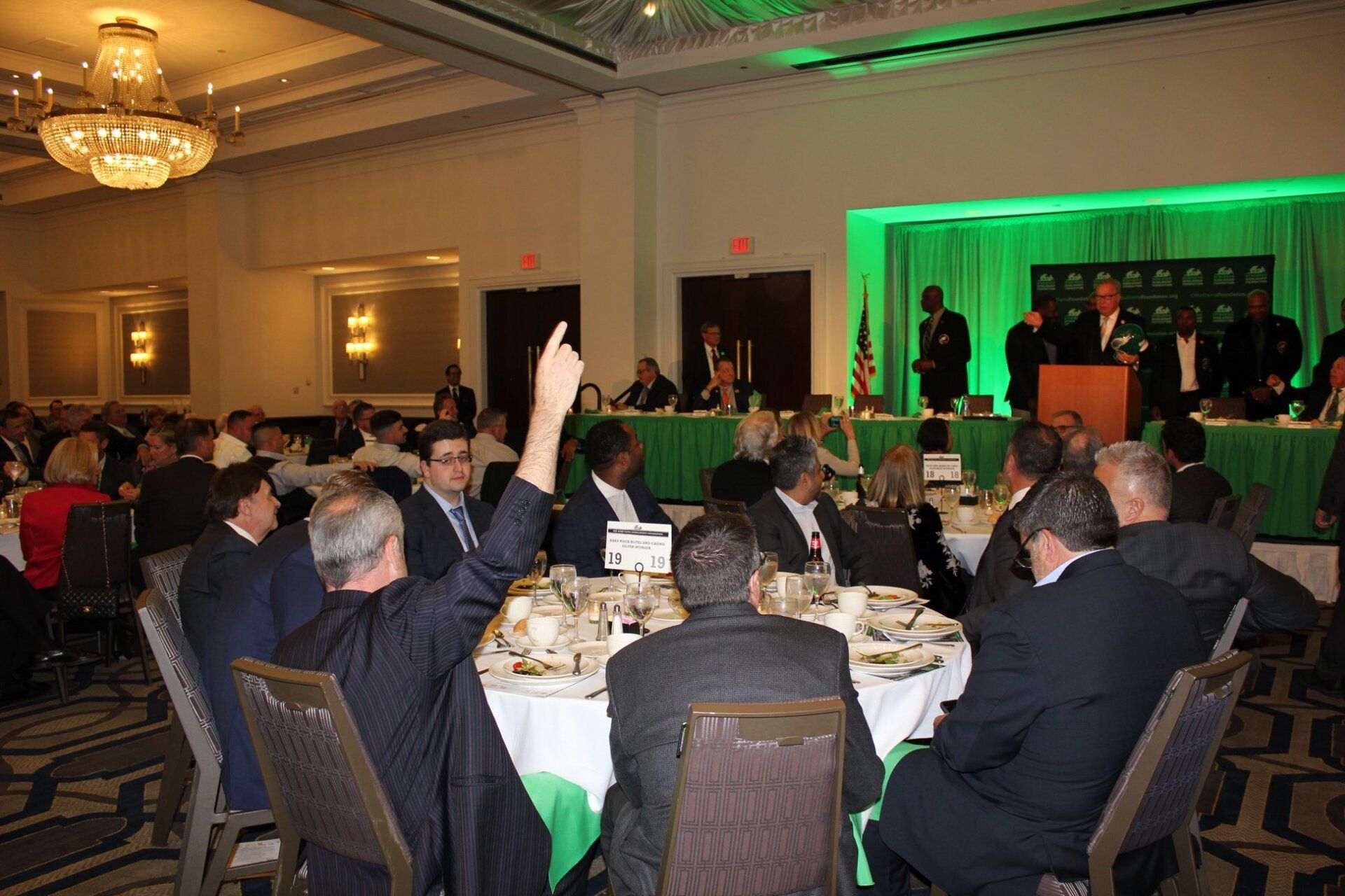 A group of people are sitting at tables with their hands up.
