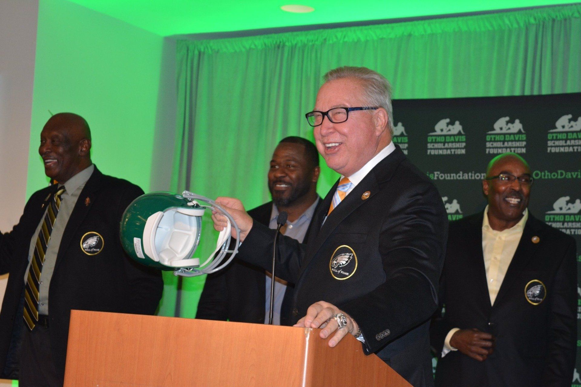 A man in a suit is standing at a podium holding a helmet.